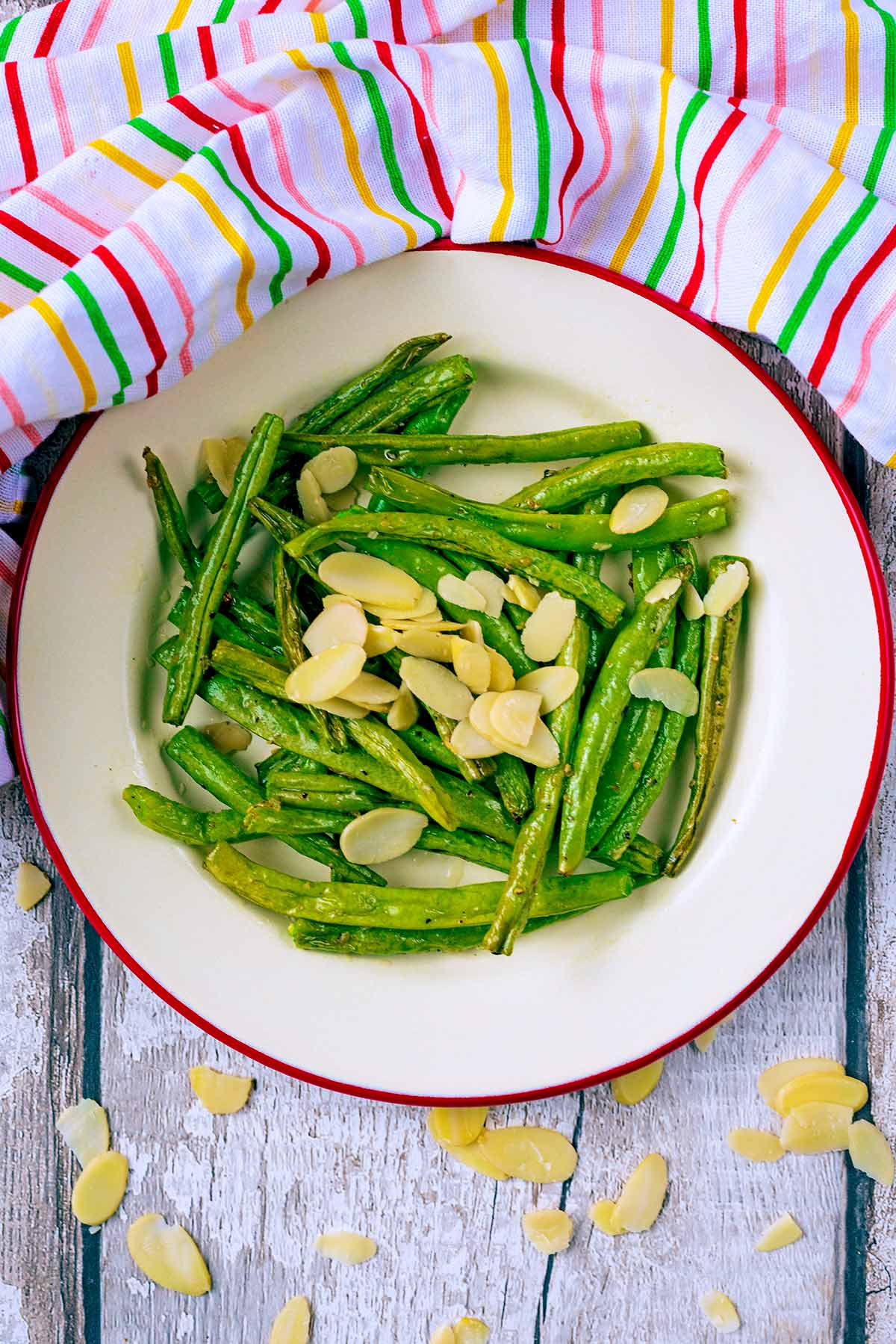 A plate of cooked green beans with almond flakes on top.