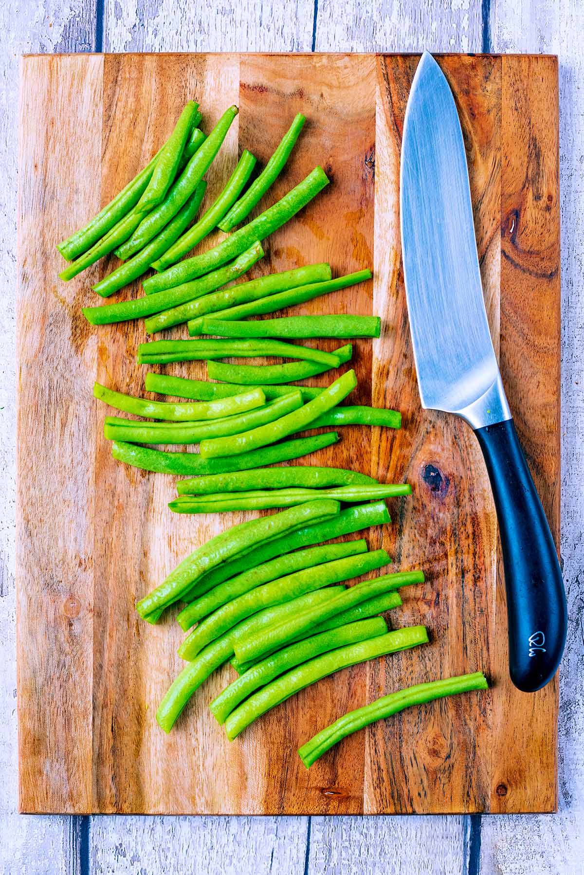 Trimmed green beans and a chef's knife on a wooden chopping board.