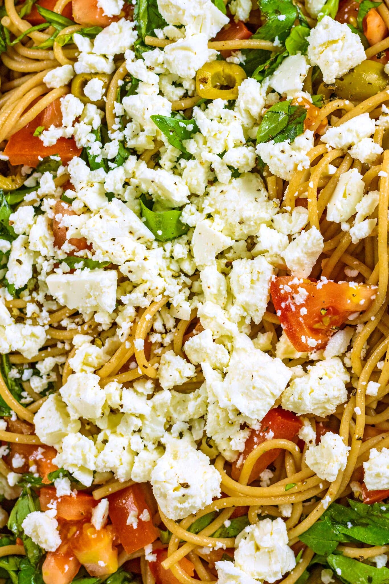 Crumbled feta on top of spaghetti, tomatoes, olives and basil.