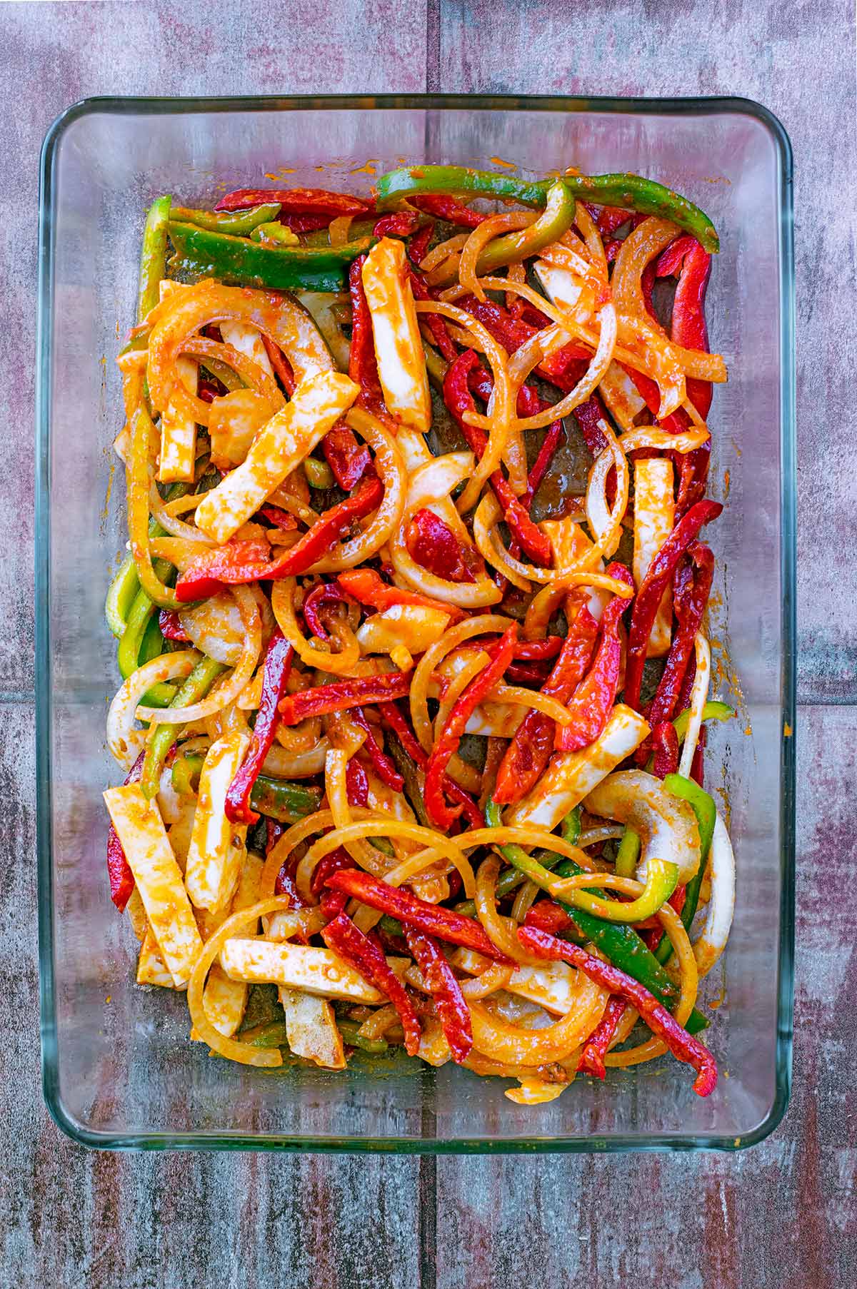 A large glass baking dish containing sliced peppers, onions and halloumi, all covered in fajita seasoning.