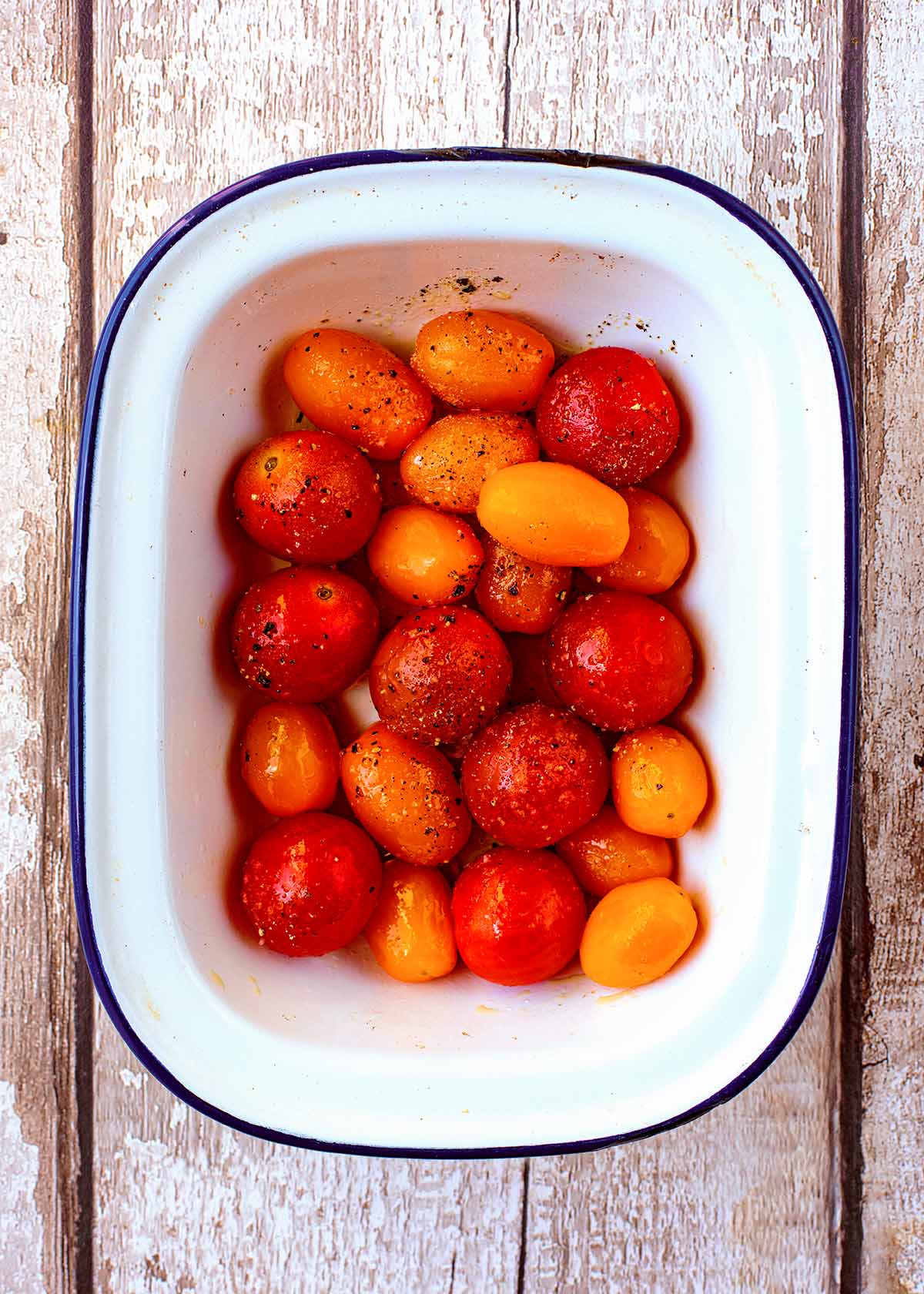 Red and orange cherry tomatoes in a white baking dish.