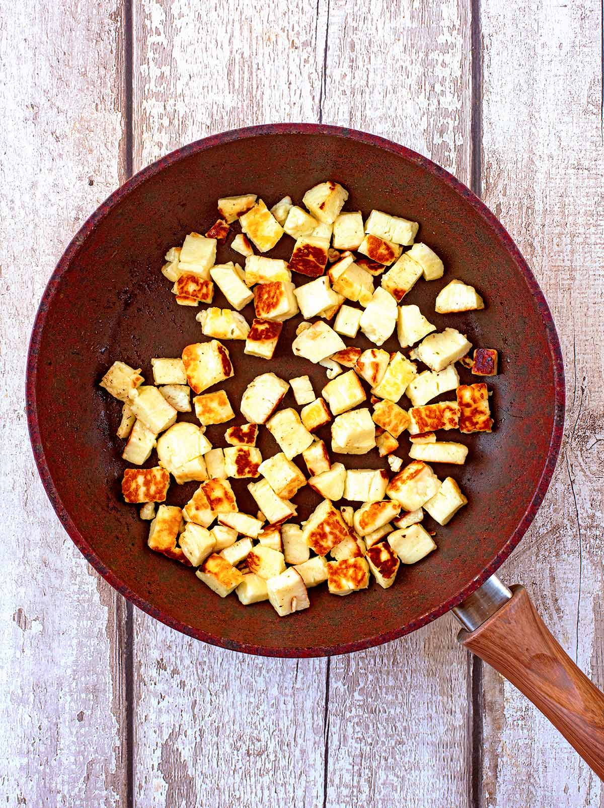 A brown frying pan with cubes of halloumi cooking in it.