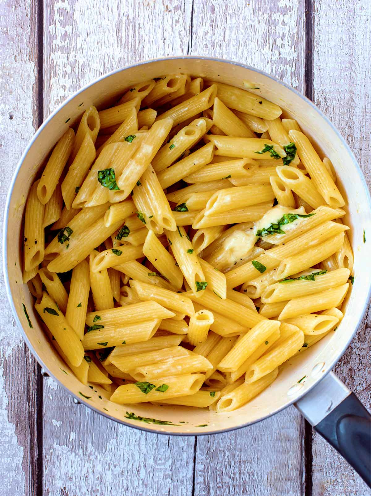 A saucepan full of cooked penne pasta in a cream cheese sauce.