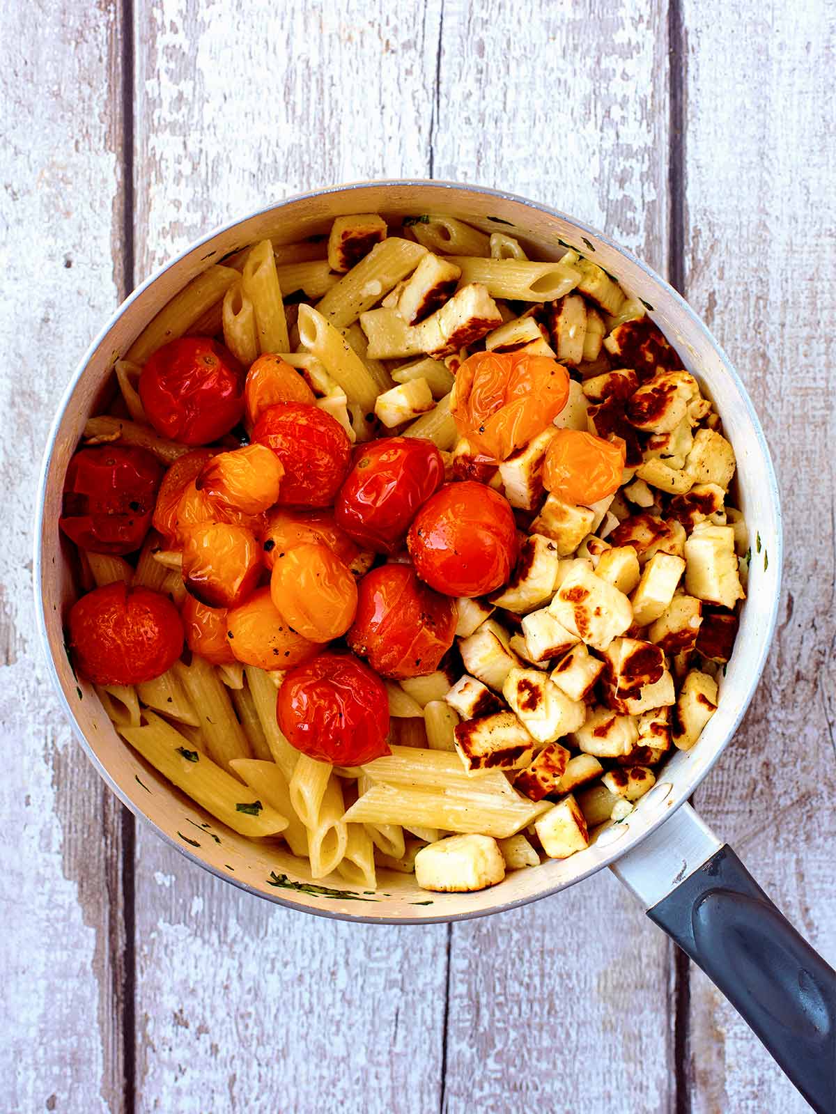 A saucepan filled with creamy penne pasta, cherry tomatoes and cooked cubes of halloumi.