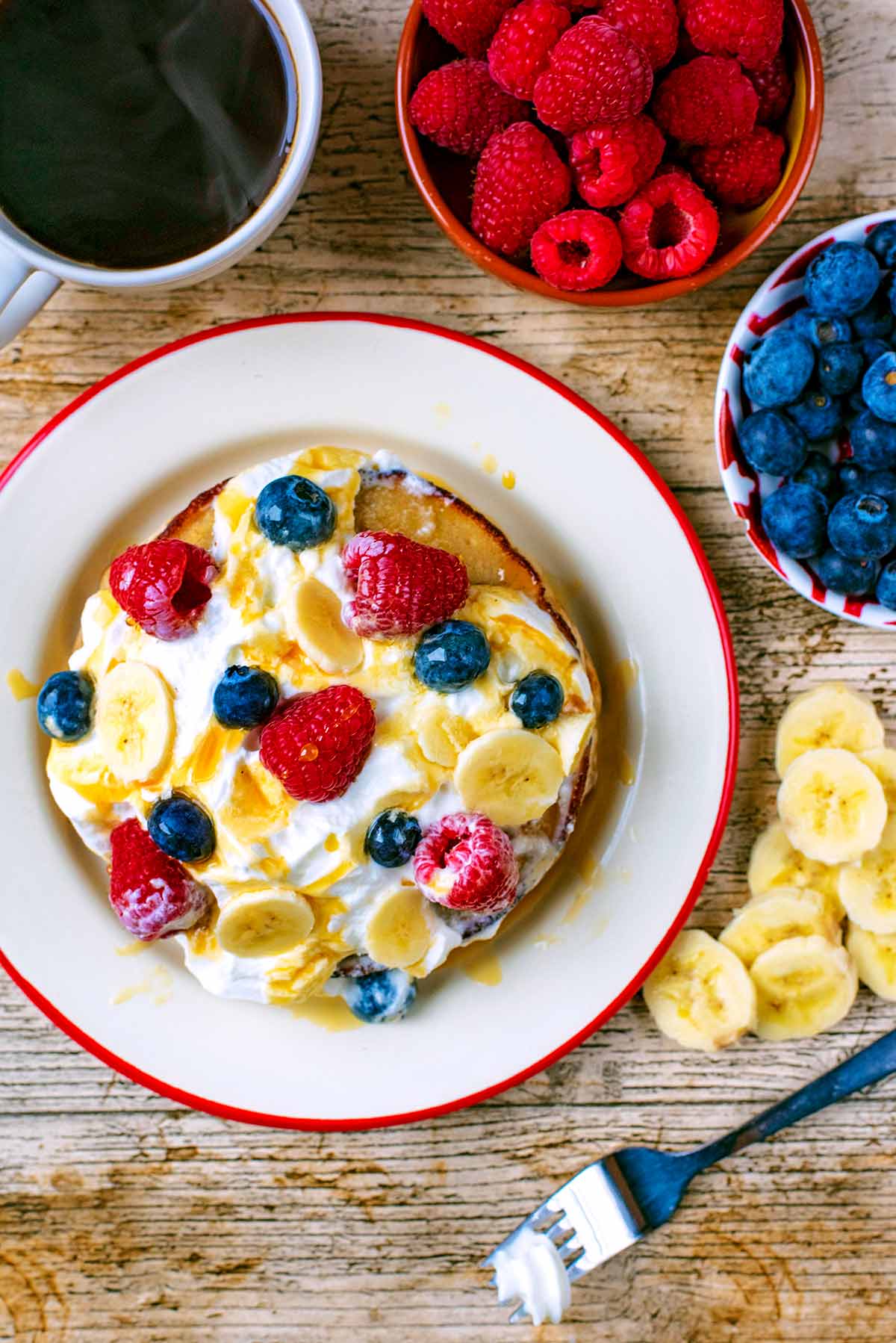 A stack of banana pancakes on a plate with berries and banana next to them.