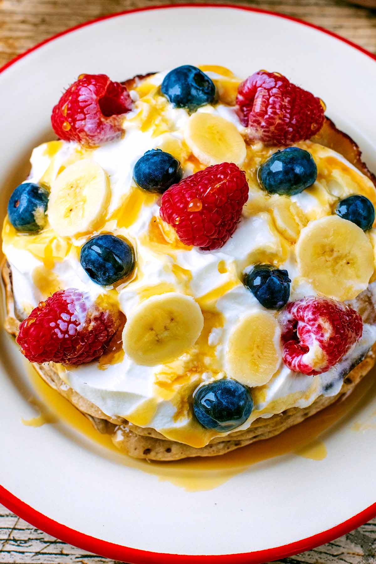 Cream topped banana pancakes with blueberries, raspberries and sliced banana.