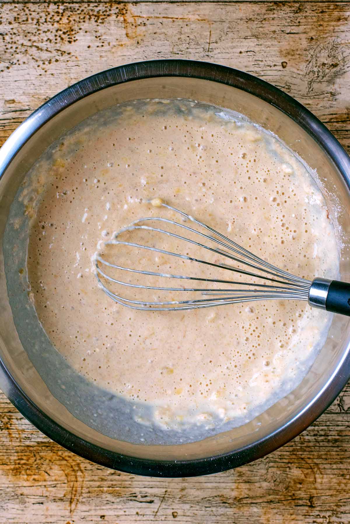 A mixing bowl containing mixed pancake batter and a whisk.