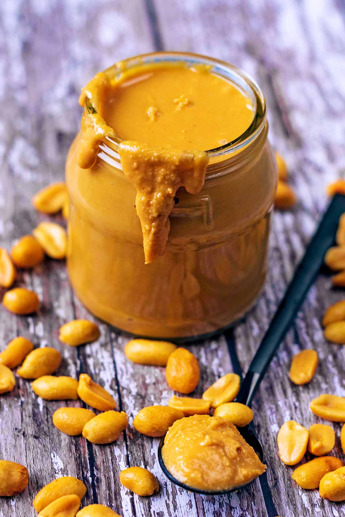 A jar of peanut butter surrounded by peanuts.