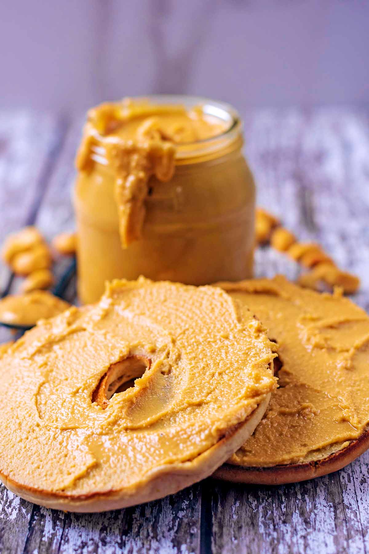 Two bagel halves smothered in peanut butter in front of a jar of peanut butter.