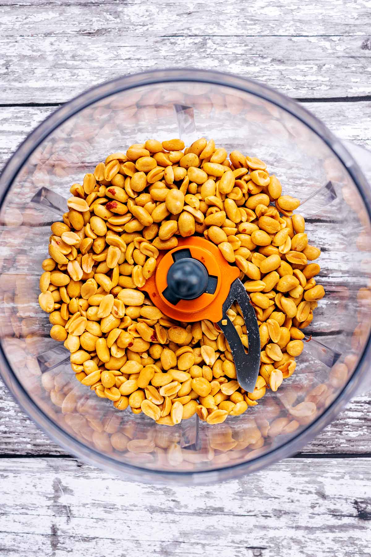 A food processor bowl containing loads of peanuts.