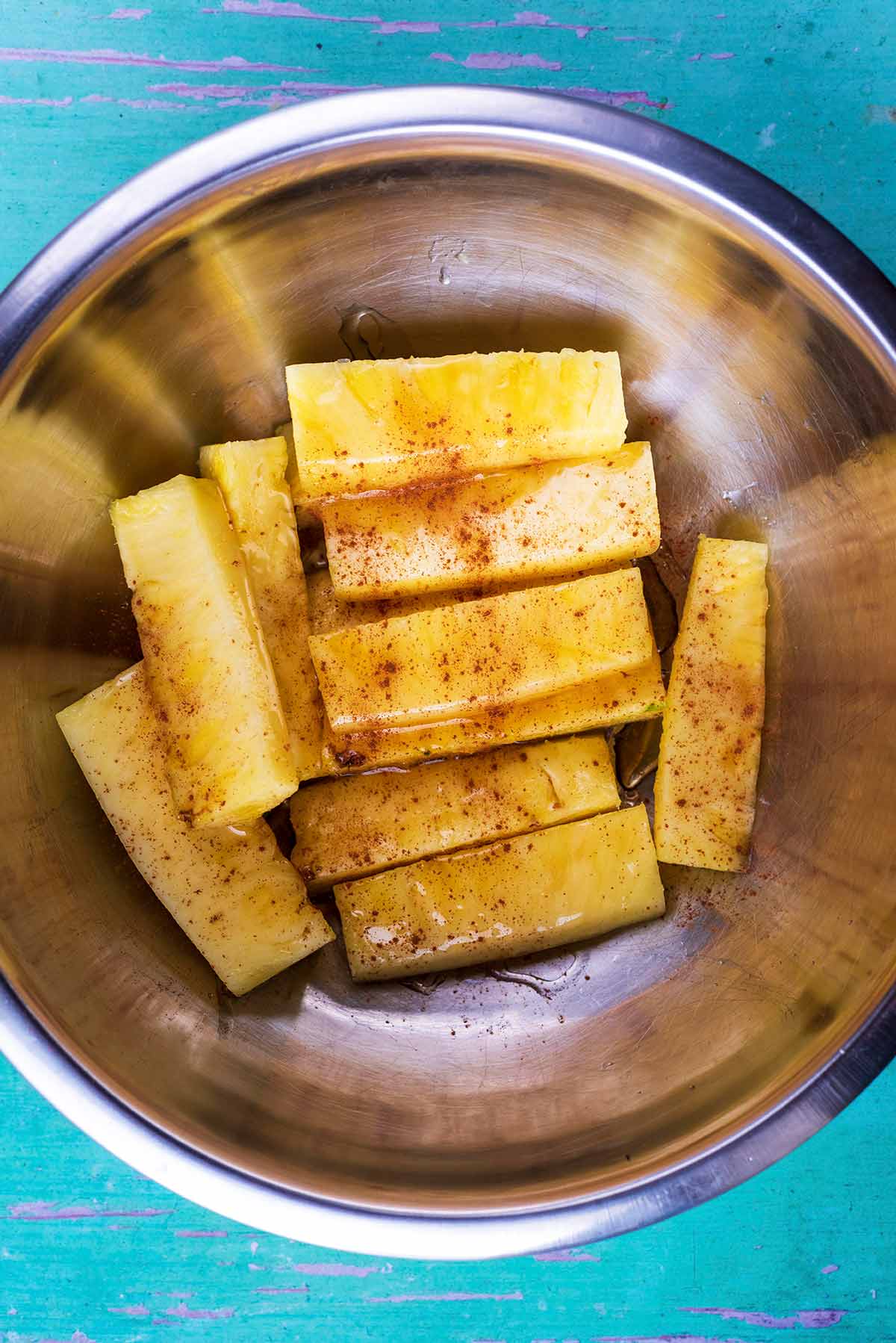 A mixing bowl containing sticks of pineapple covered in honey and cinnamon.
