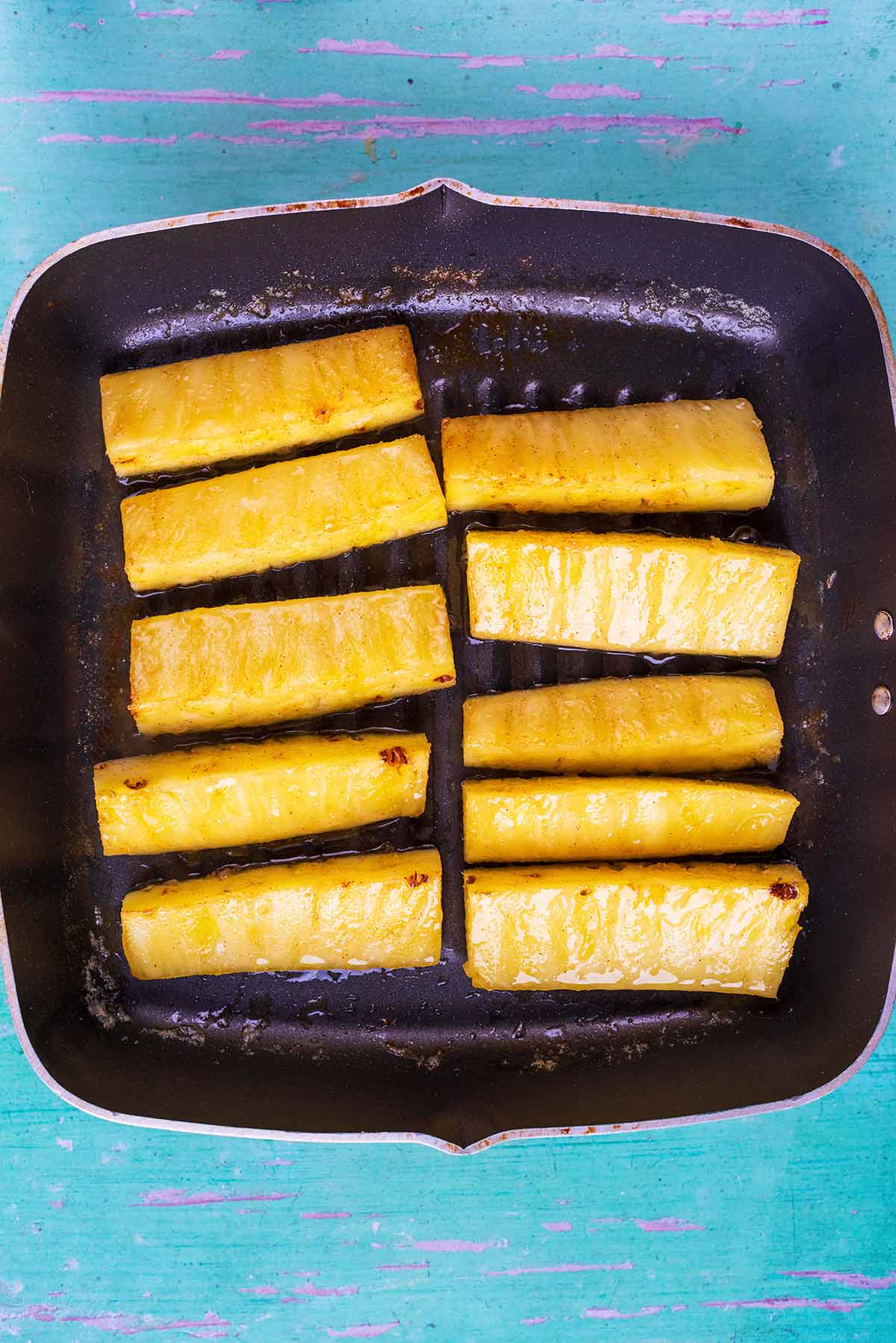 A griddle pan with pineapple sticks on it.