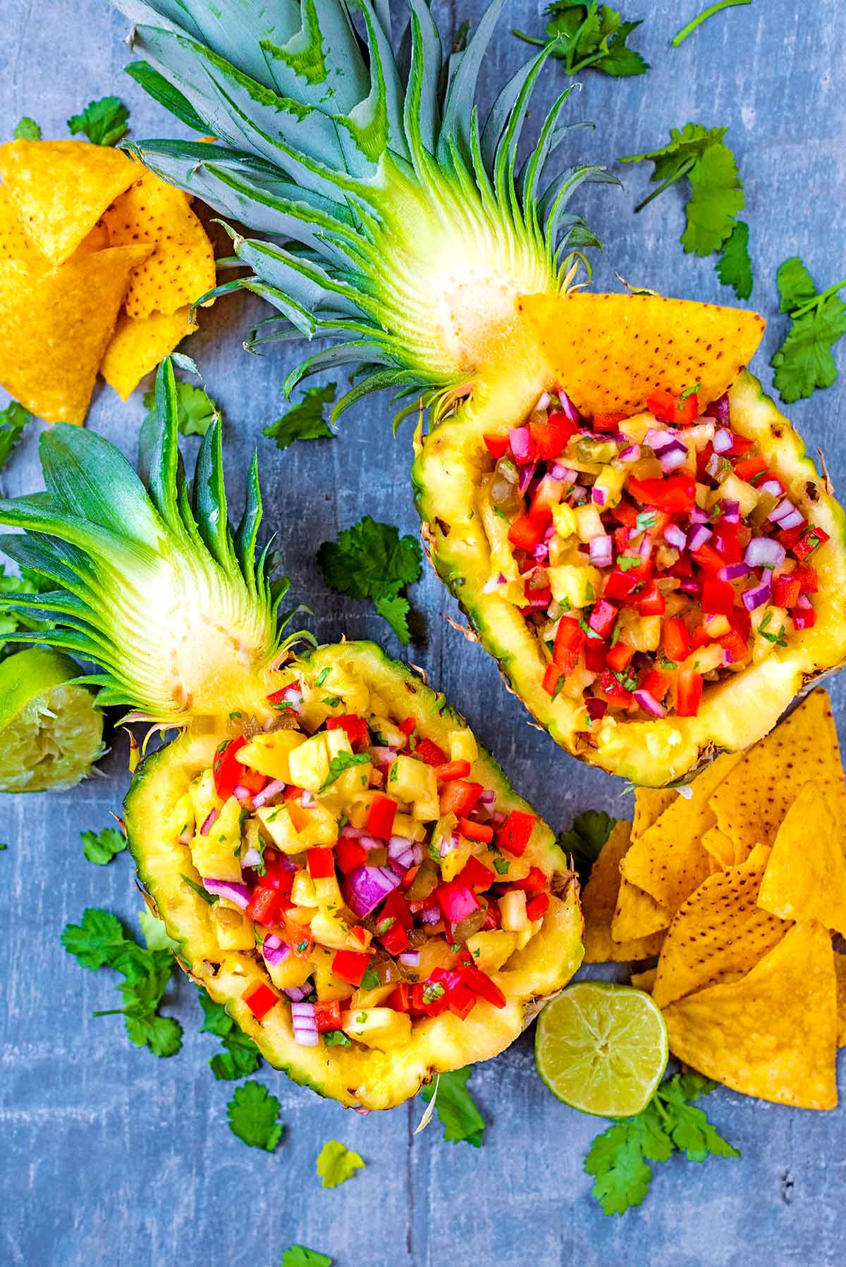 A pineapple sliced in half and filled with salsa. Tortilla chips are scattered around.