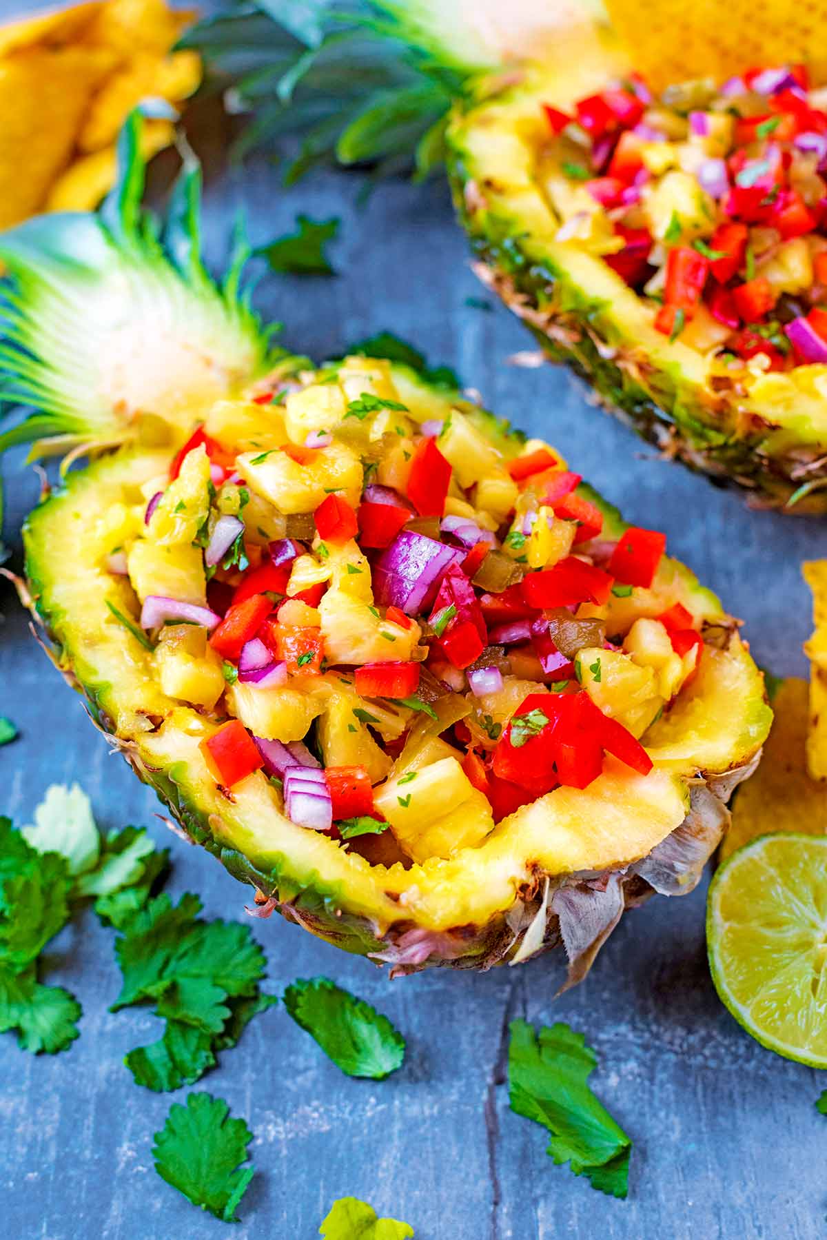 A pineapple boat filled with salsa, surrounded by chopped herbs.