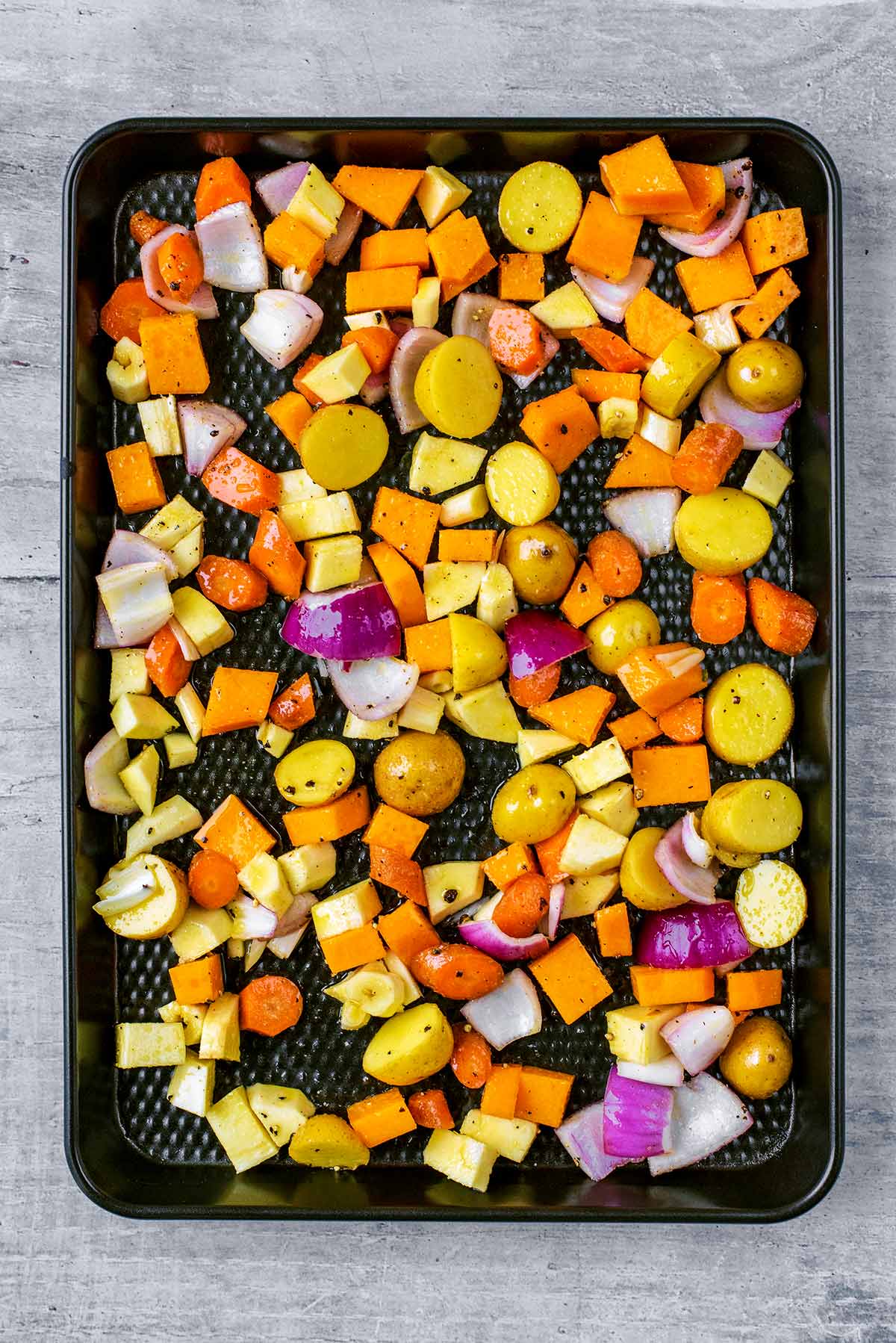 A baking tray with chopped vegetables covering it.