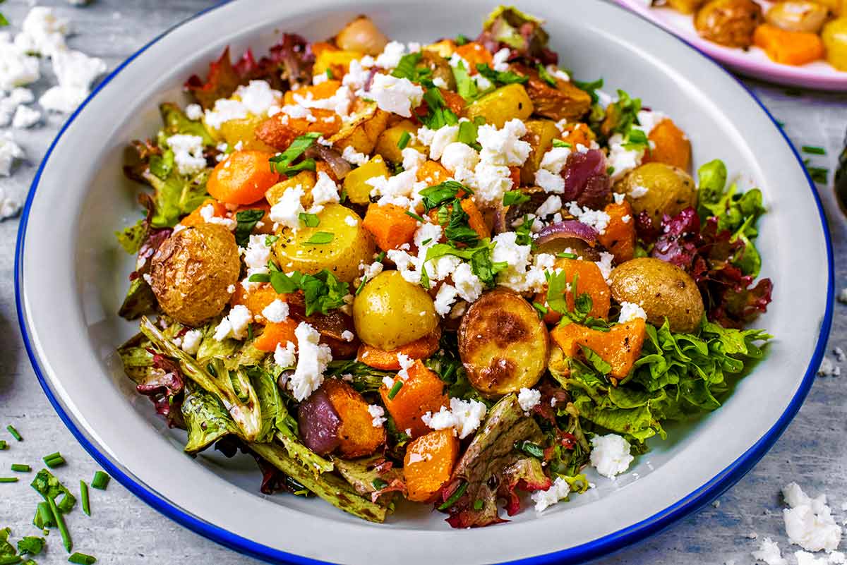 A white dish with salad leaves, roasted vegetables and feta cheese.
