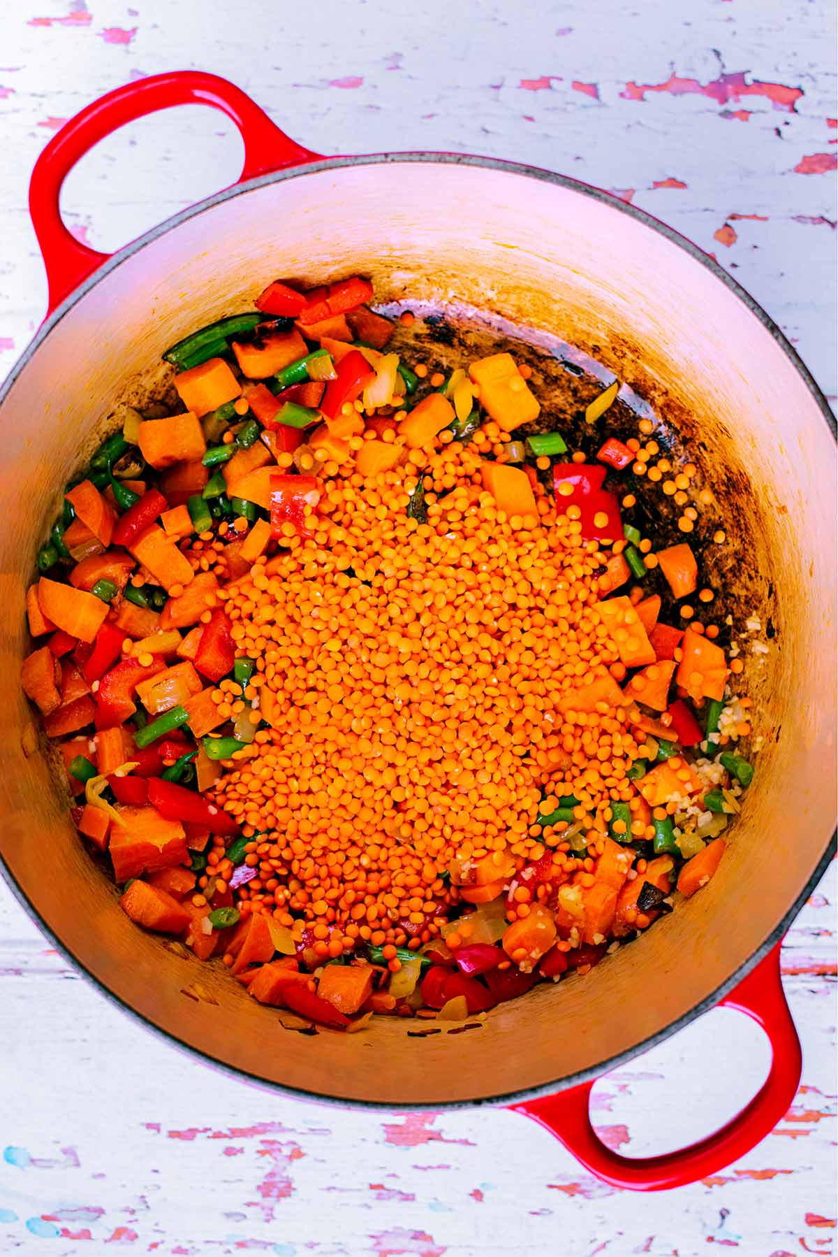 Chopped vegetables and red lentils cooking in a large pot.