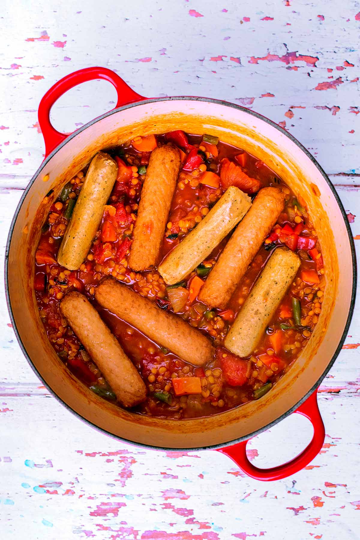 Sausages, lentils and vegetables cooking in a large red pot.