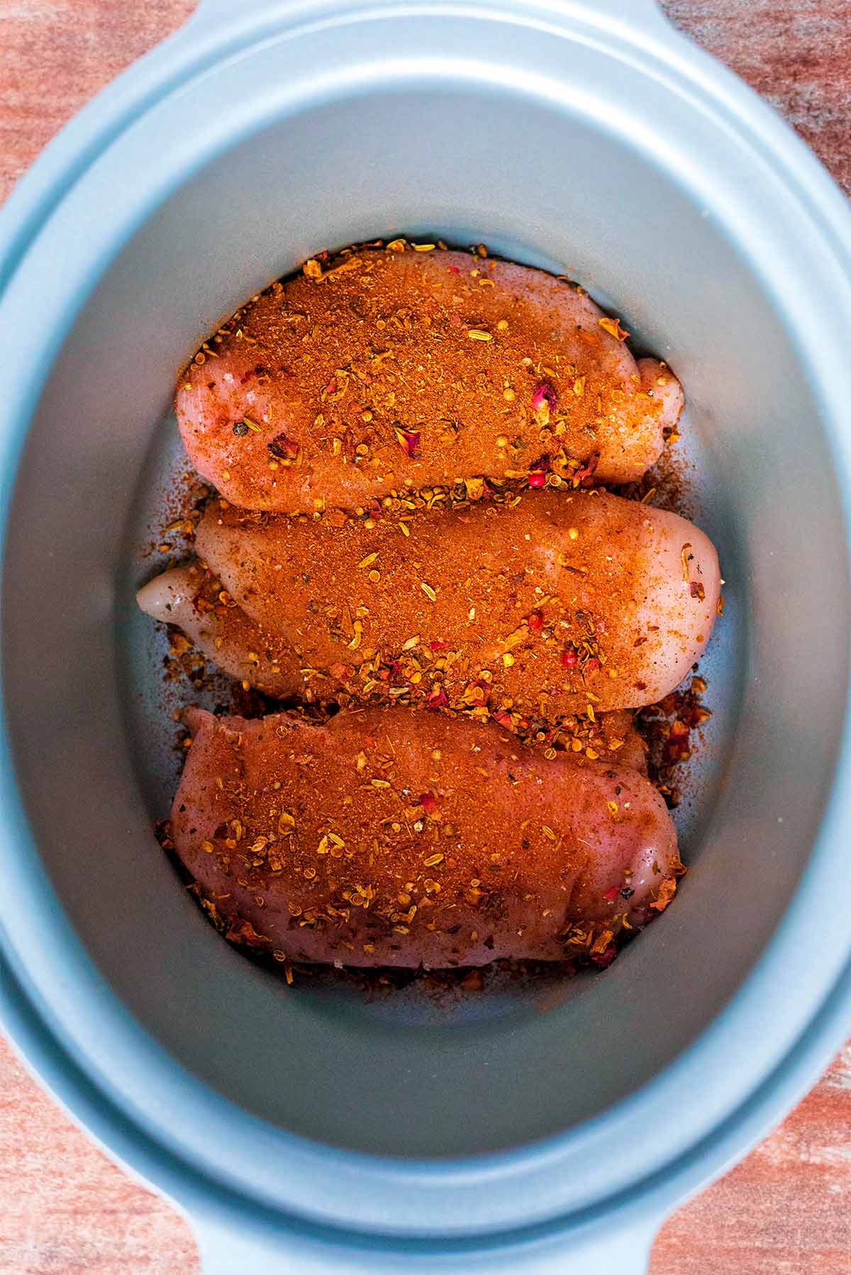 A slow cooker bowl with three chicken breasts covered in ras-el-hanout.