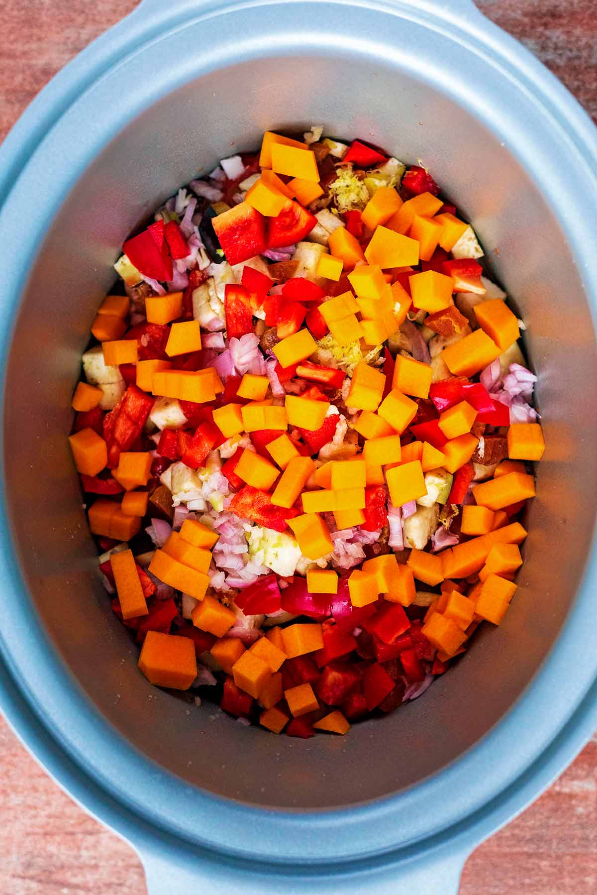 A slow cooker bowl containing chicken breasts and chopped vegetables.