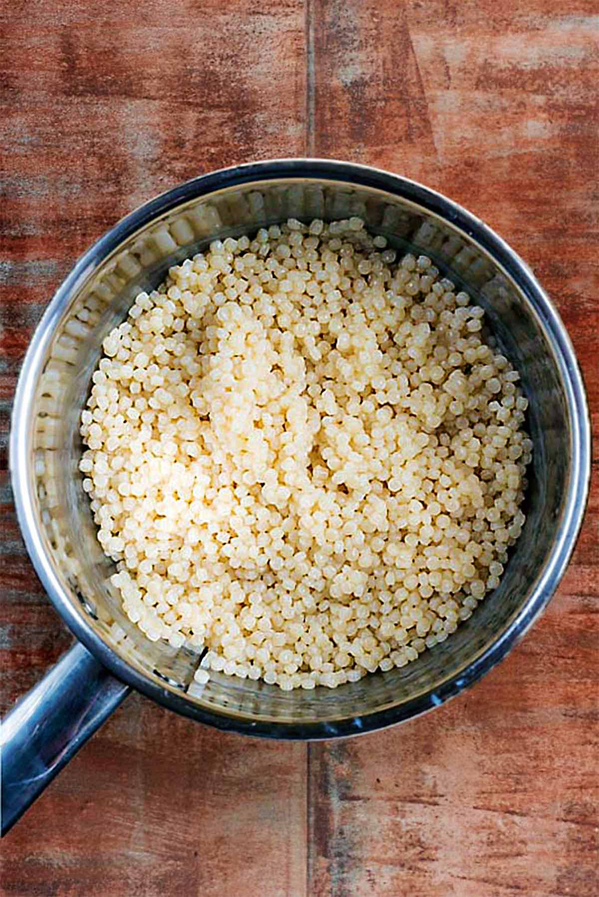 A stainless steel saucepan containing cooled Israeli couscous.