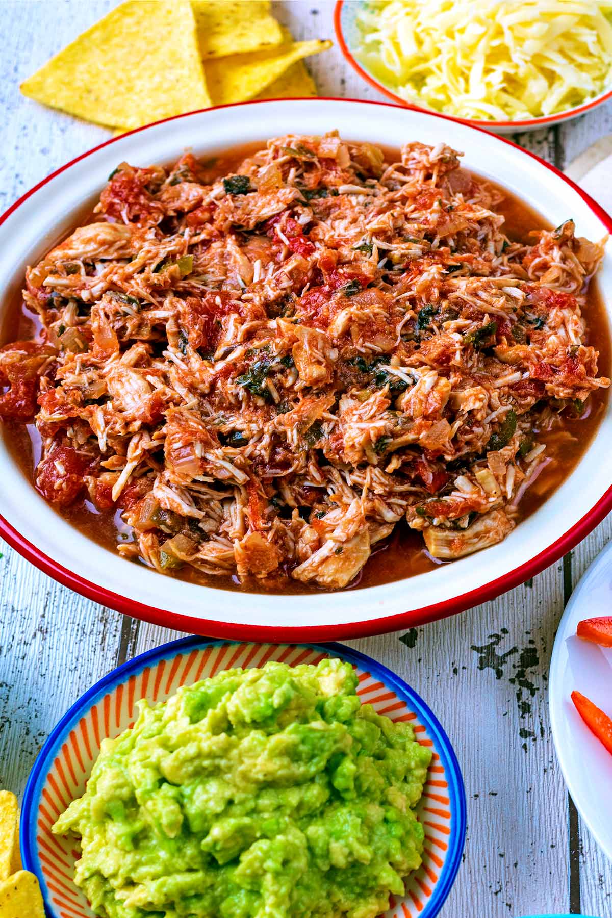 A bowl of salsa chicken next to a small dish of guacamole.