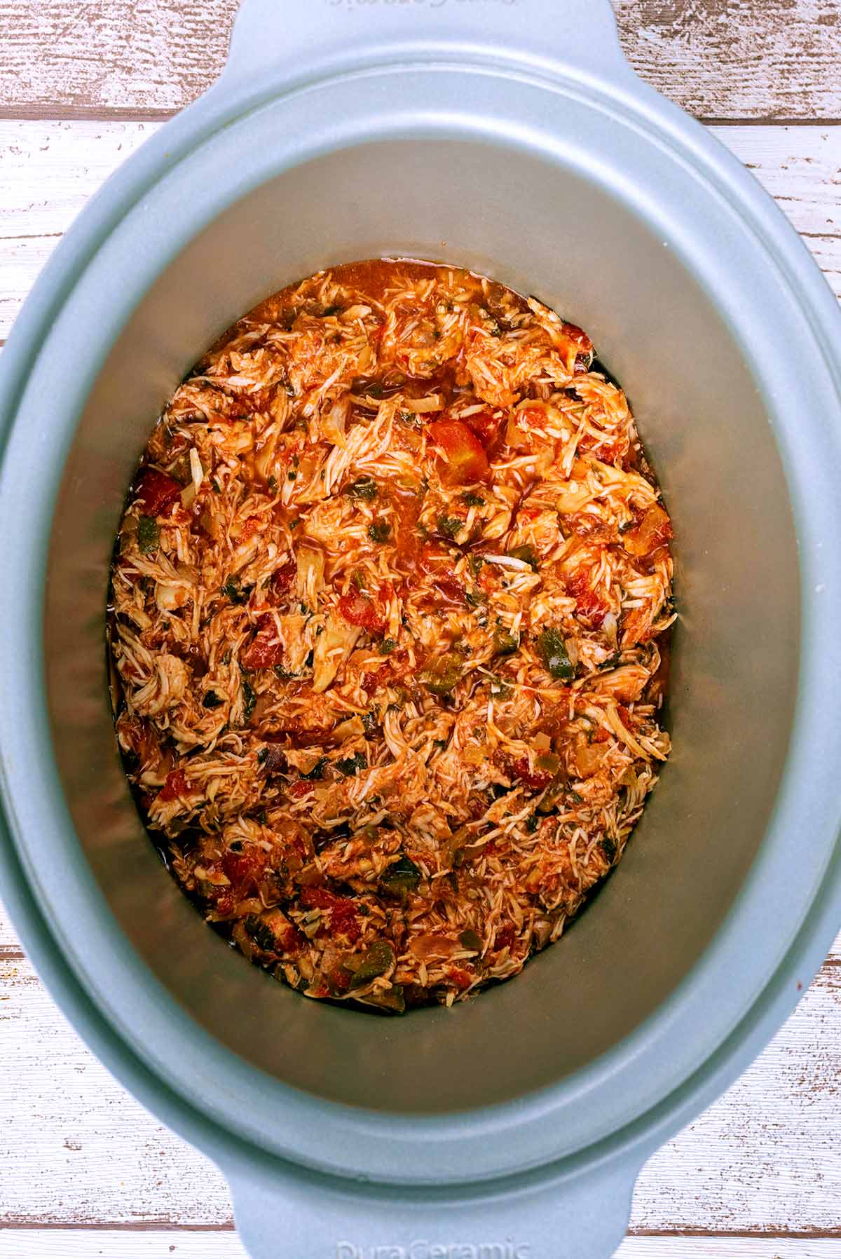 A slow cooker pot containing shredded chicken in a tomato sauce.