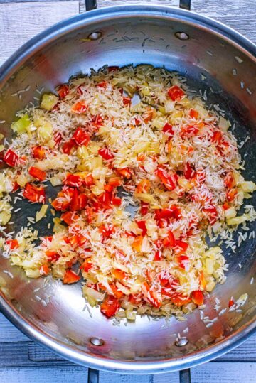 a large silver pan with chopped onion, red pepper and rice.
