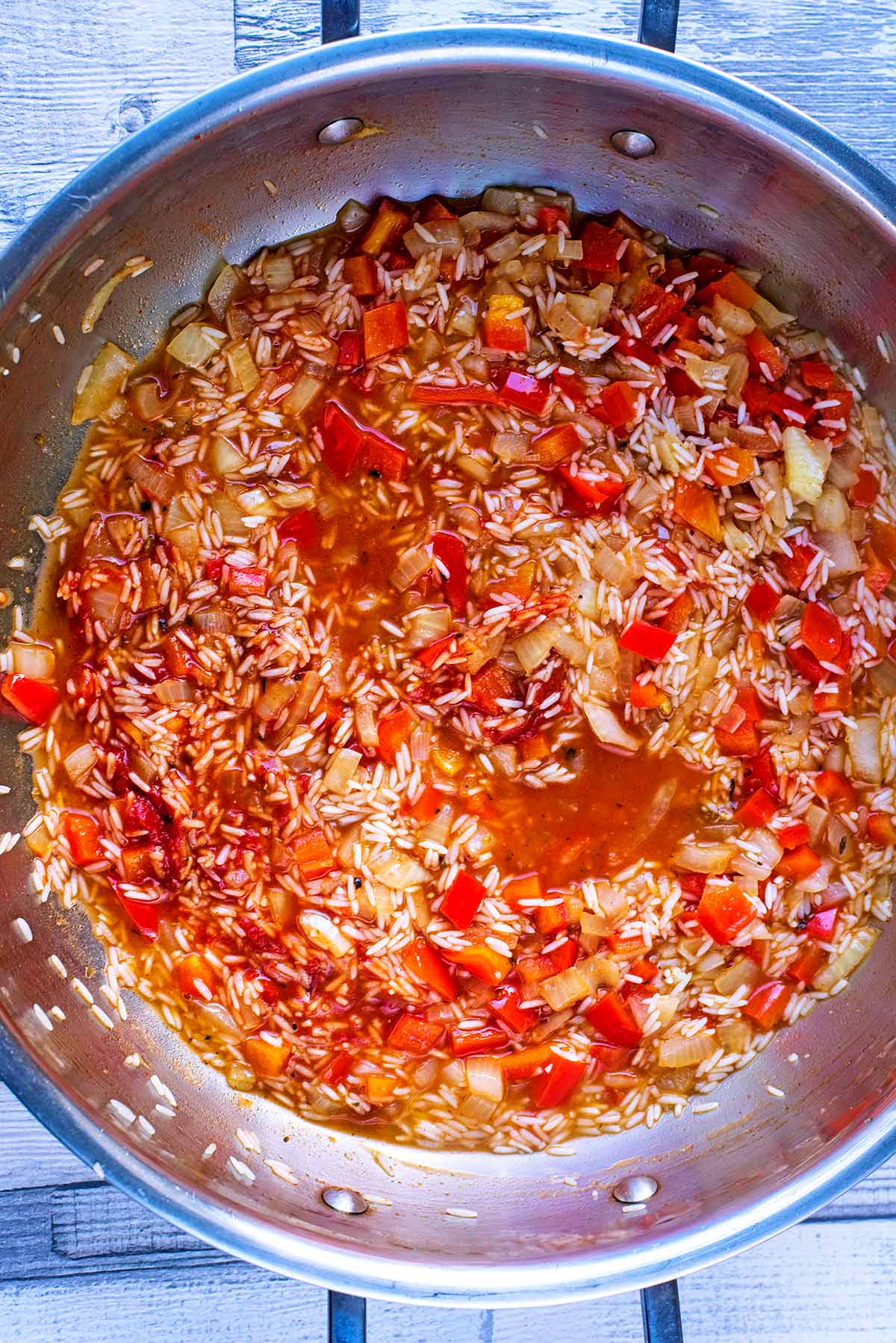 a large silver pan with chopped onion, red pepper, rice and stock.