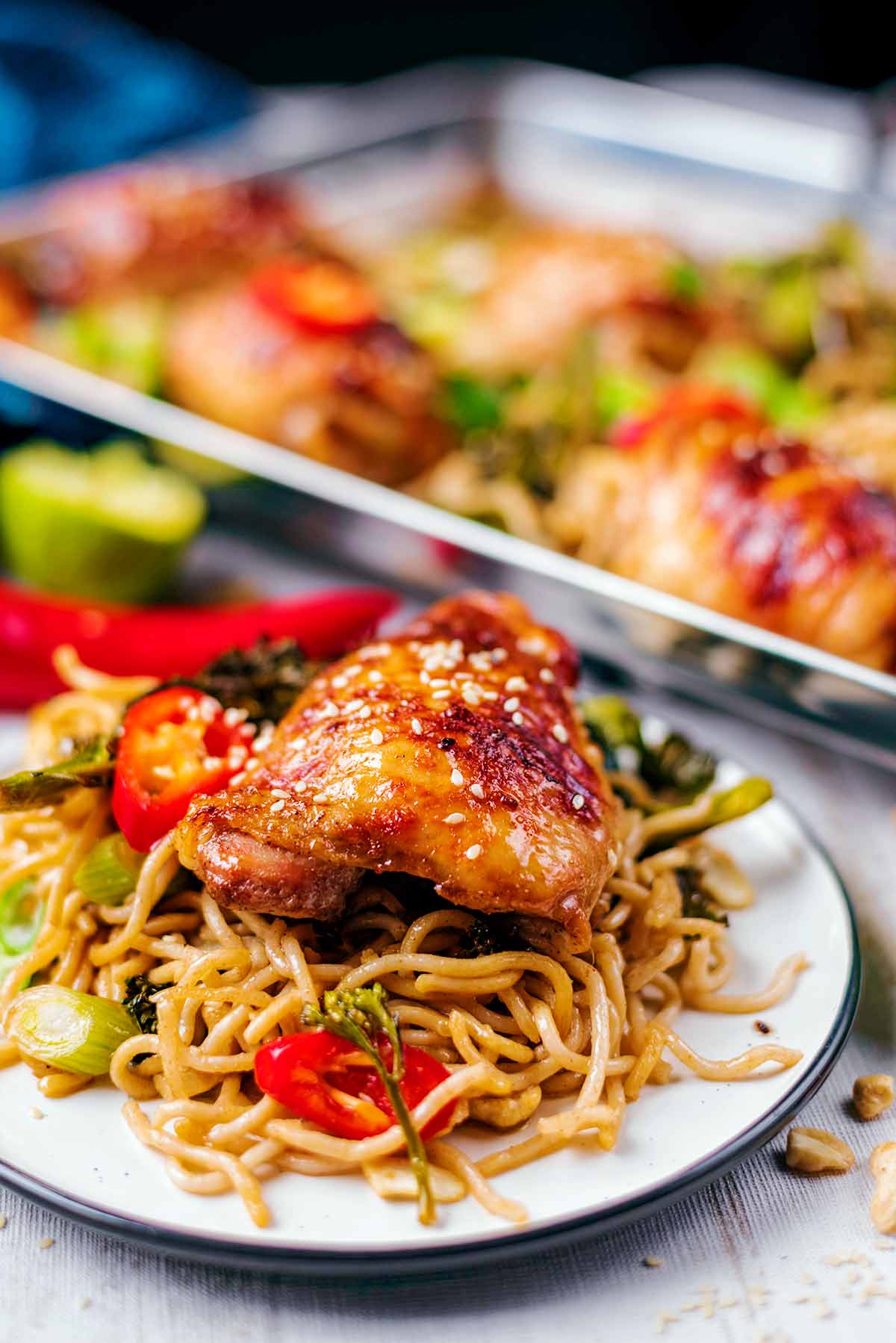 A plate of chicken and noodles in front of a tray of more chicken.