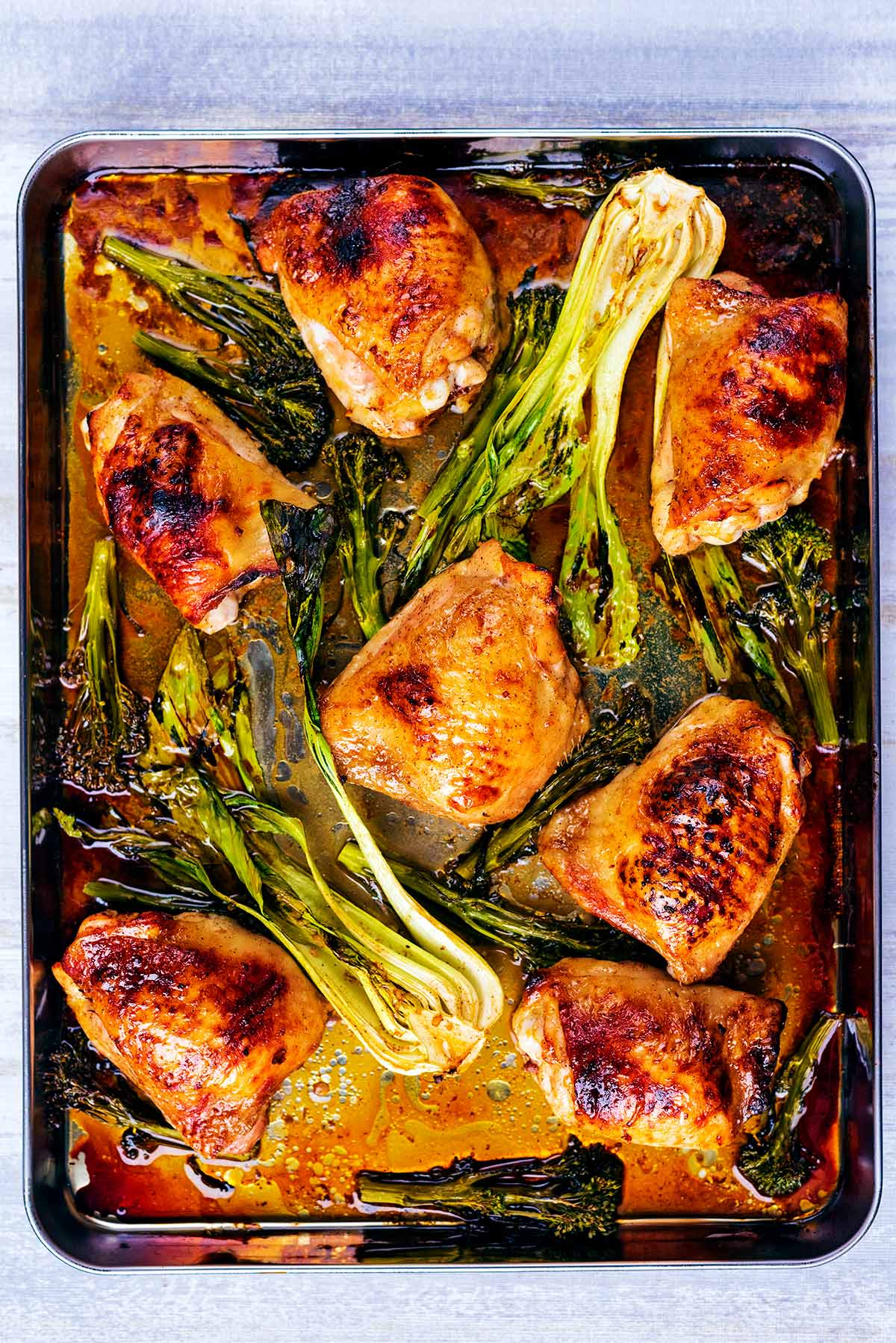 cooked chicken thighs and pak choi on a large baking tray.
