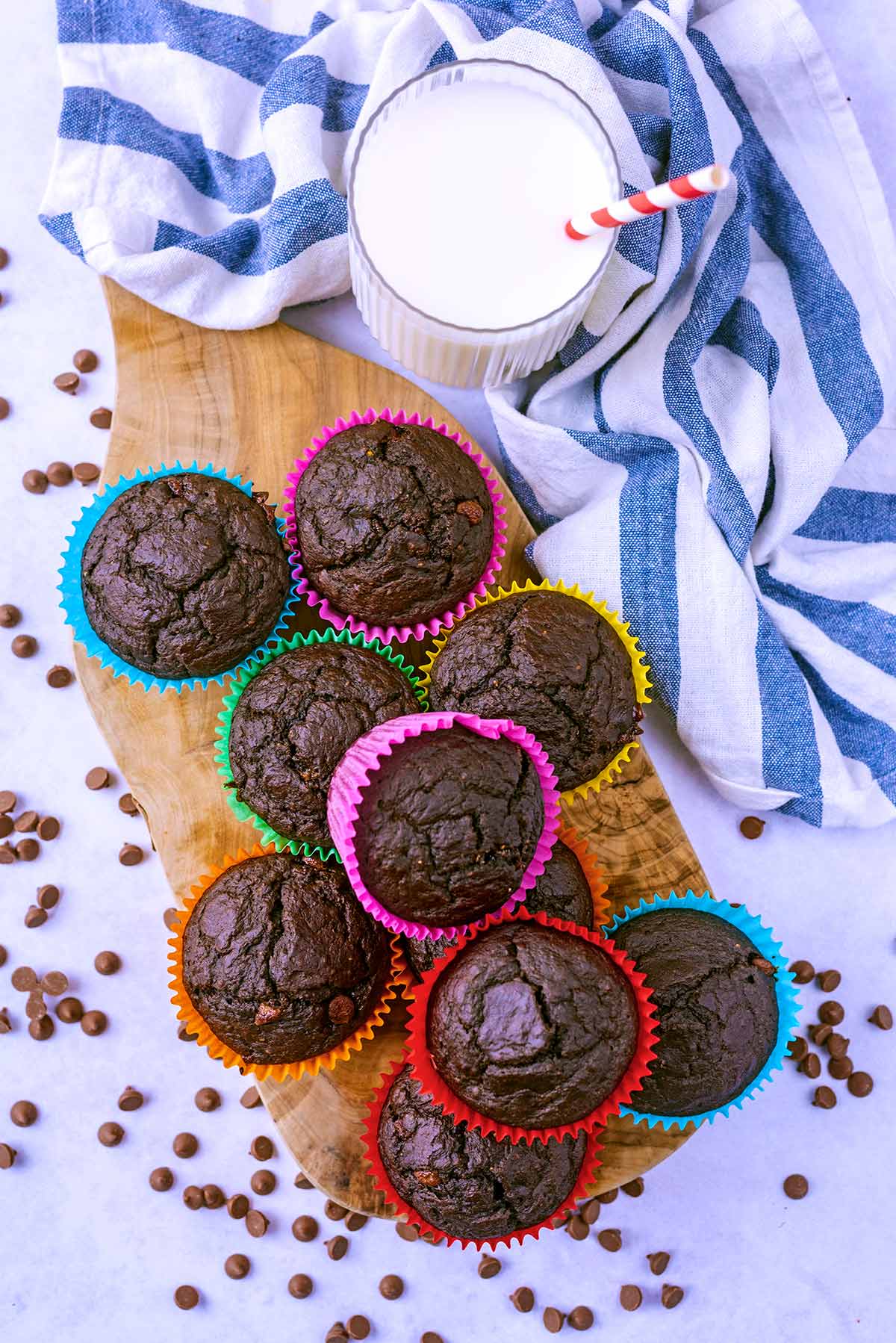 Eight chocolate muffins on a wooden serving board next to a glass of milk.