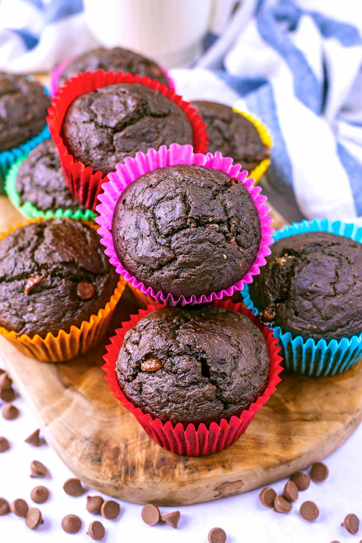 Chocolate muffins piled up on a board in front of a striped towel.