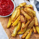 Air fryer chips on a wooden board with a bowl of ketchup.