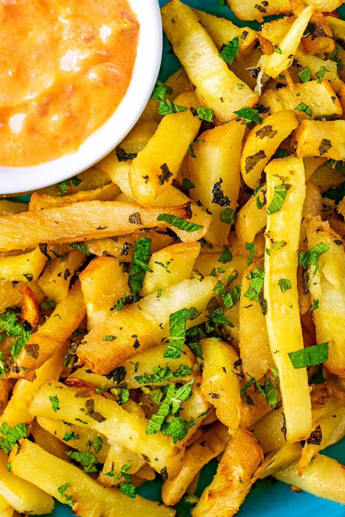 Baked Parsnip Fries on a blue plate with a small pot of chilli dip.