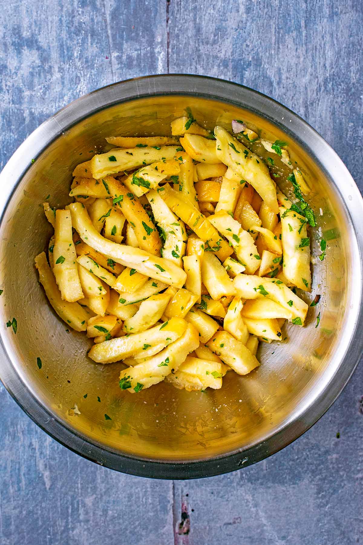 A mixing bowl containing uncooked parsnip fries with chopped herbs.