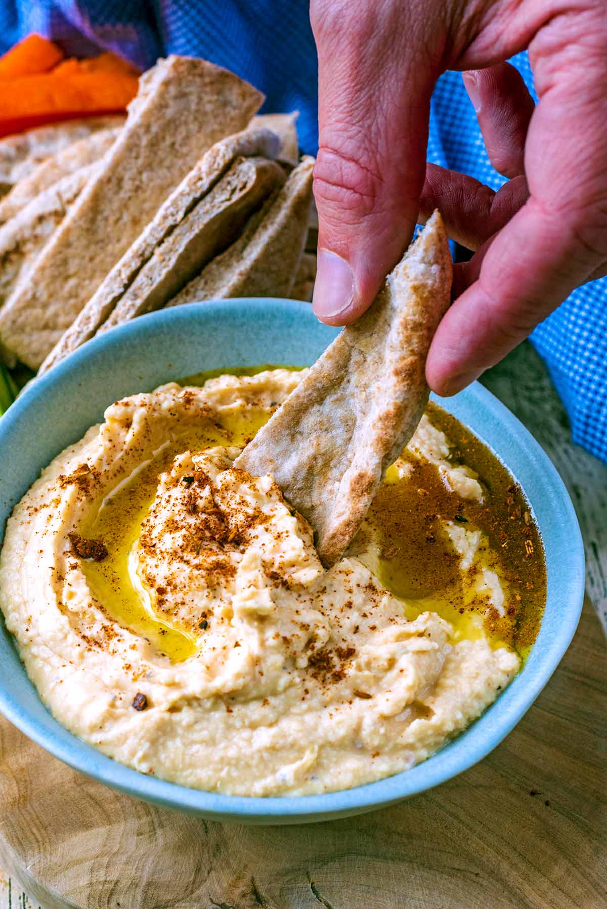 A hand dipping a piece of pita bread into some hummus.