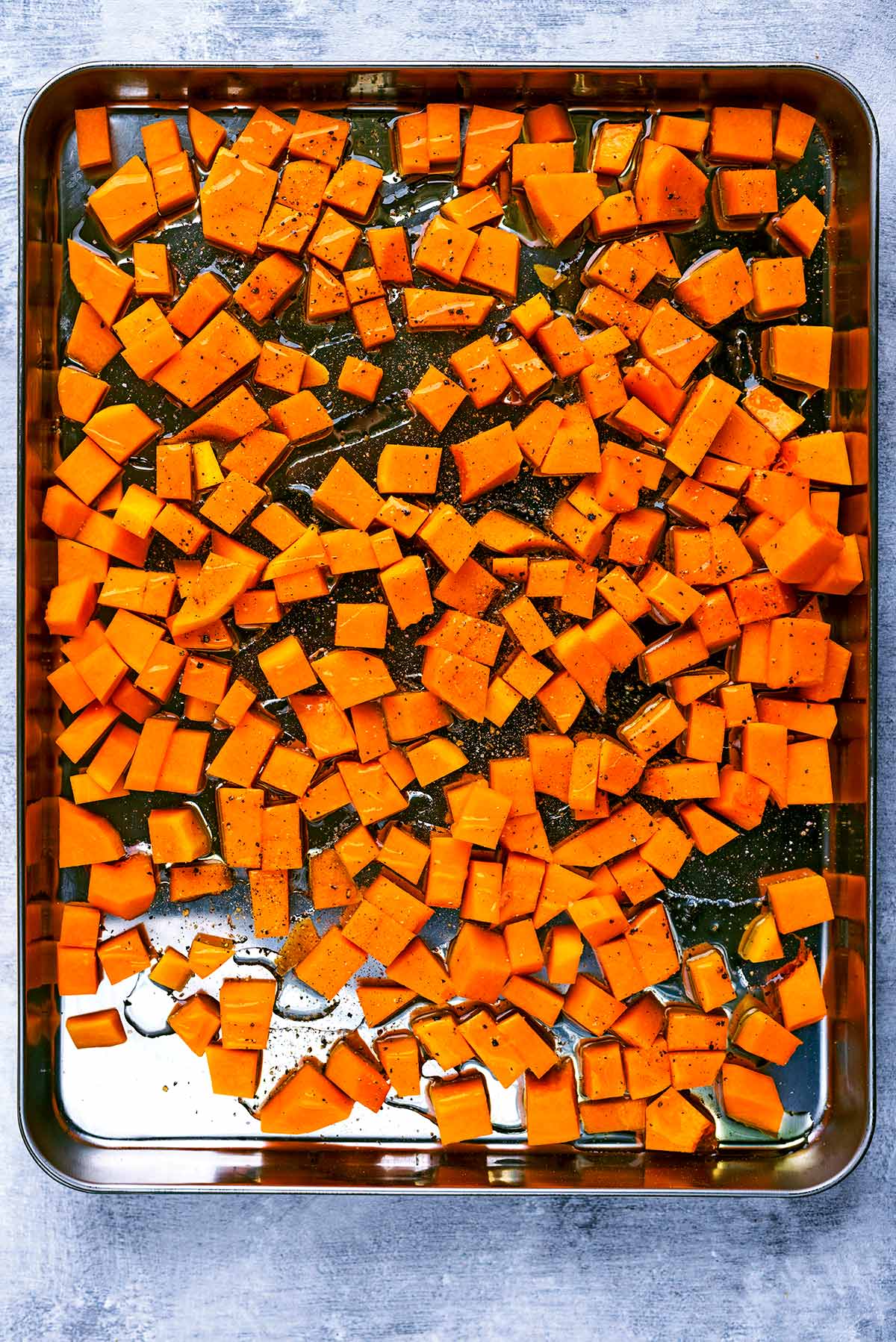 A large baking sheet covered in cubes of butternut squash.