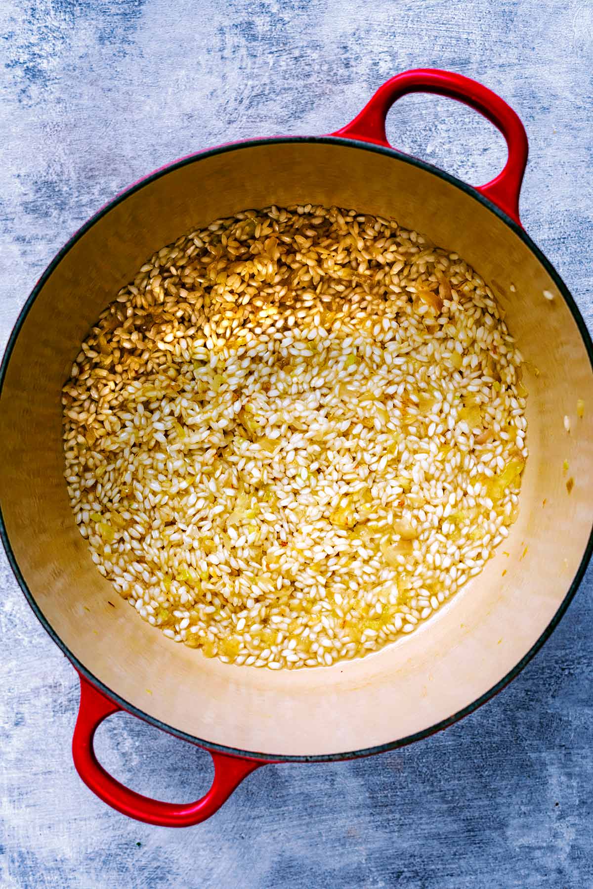 A large red pan containing risotto rice and white wine.