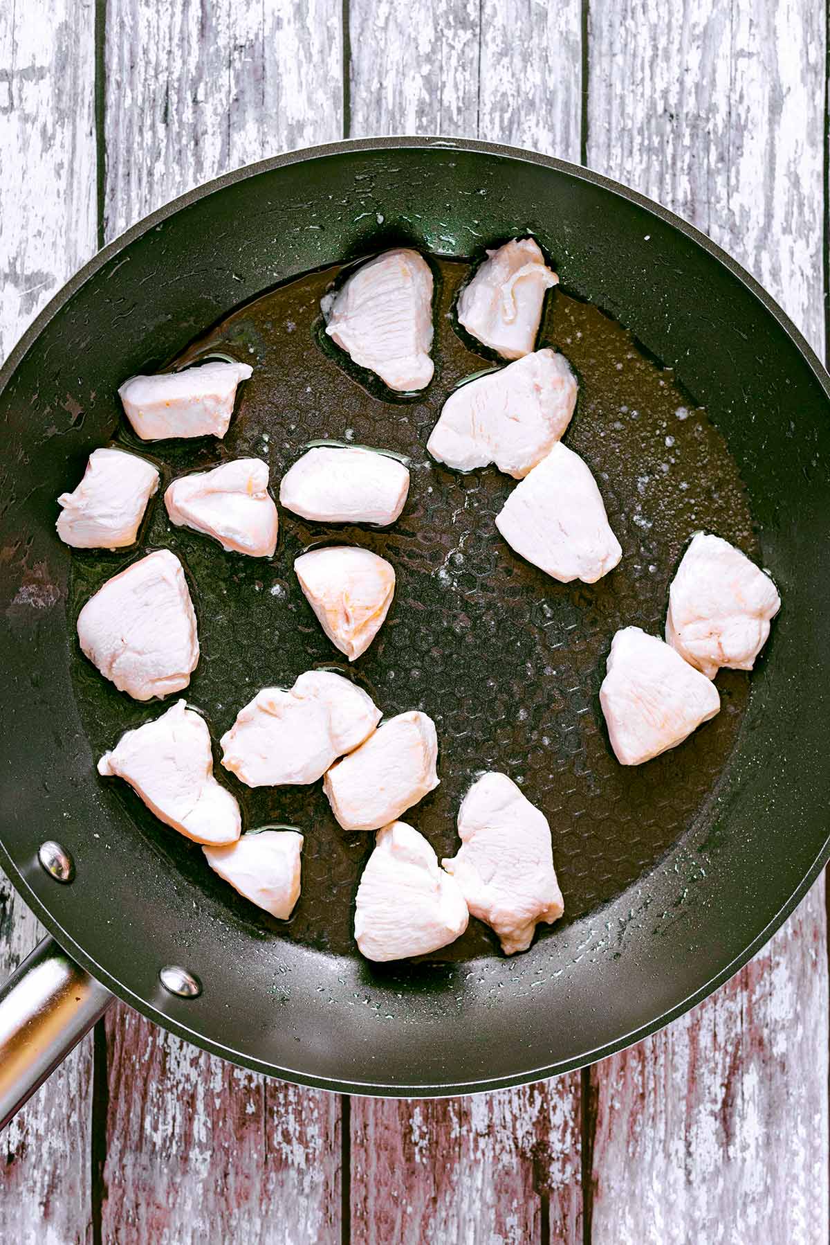 A frying pan with chunks of chicken cooking in it.