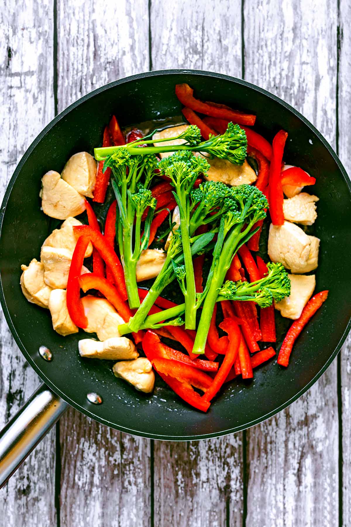 Chicken chunks, strips of red pepper and broccoli cooking in a frying pan