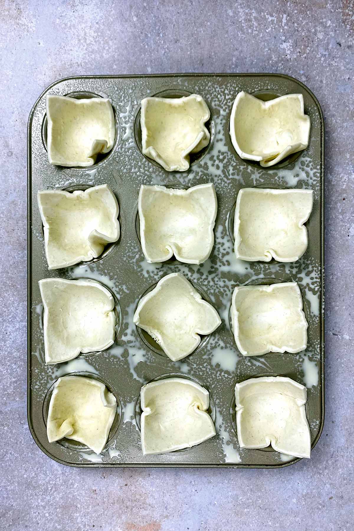 A muffin tin with squares of pastry in each hole.