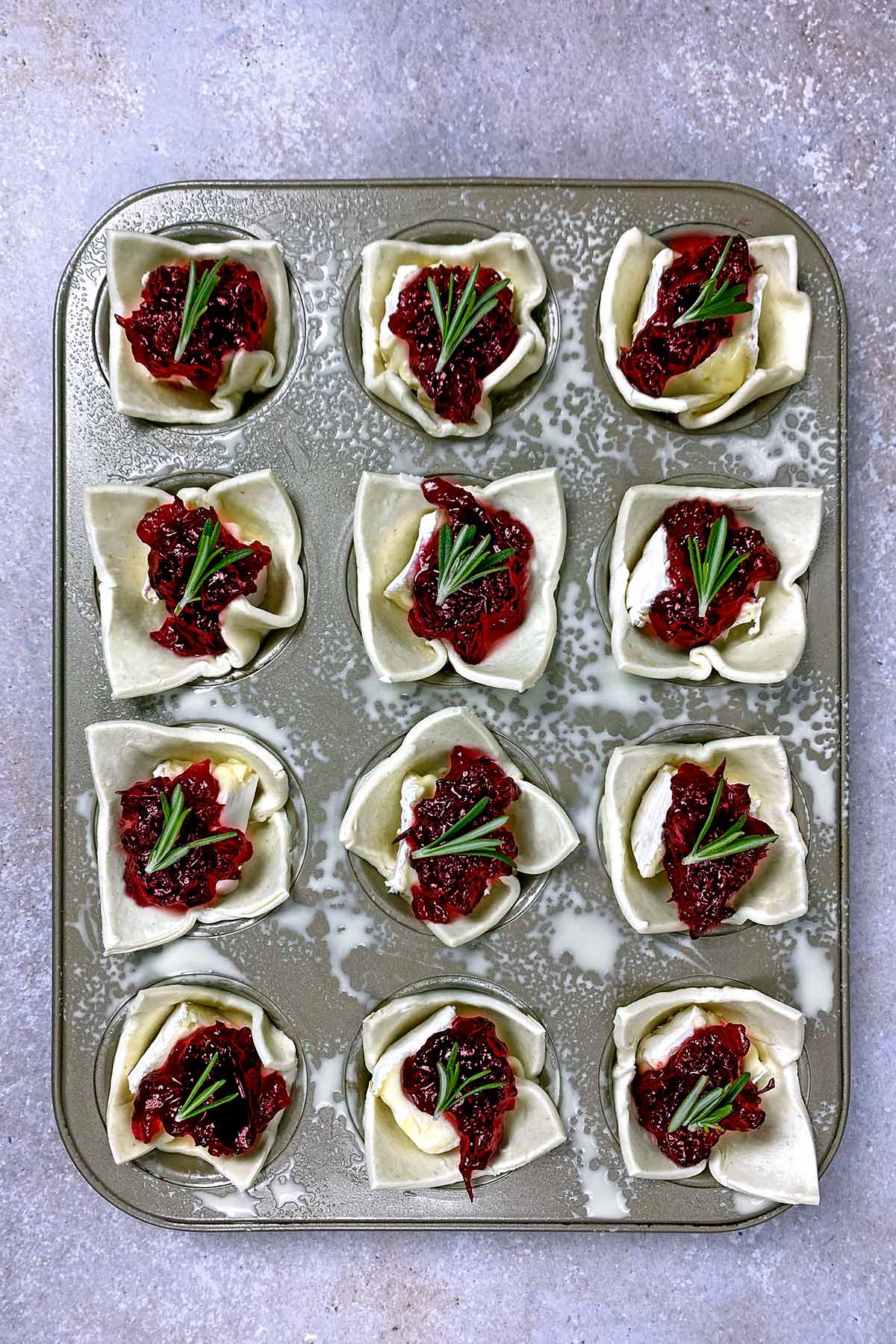 A muffin tin with pastry, brie and cranberry sauce in each hole.