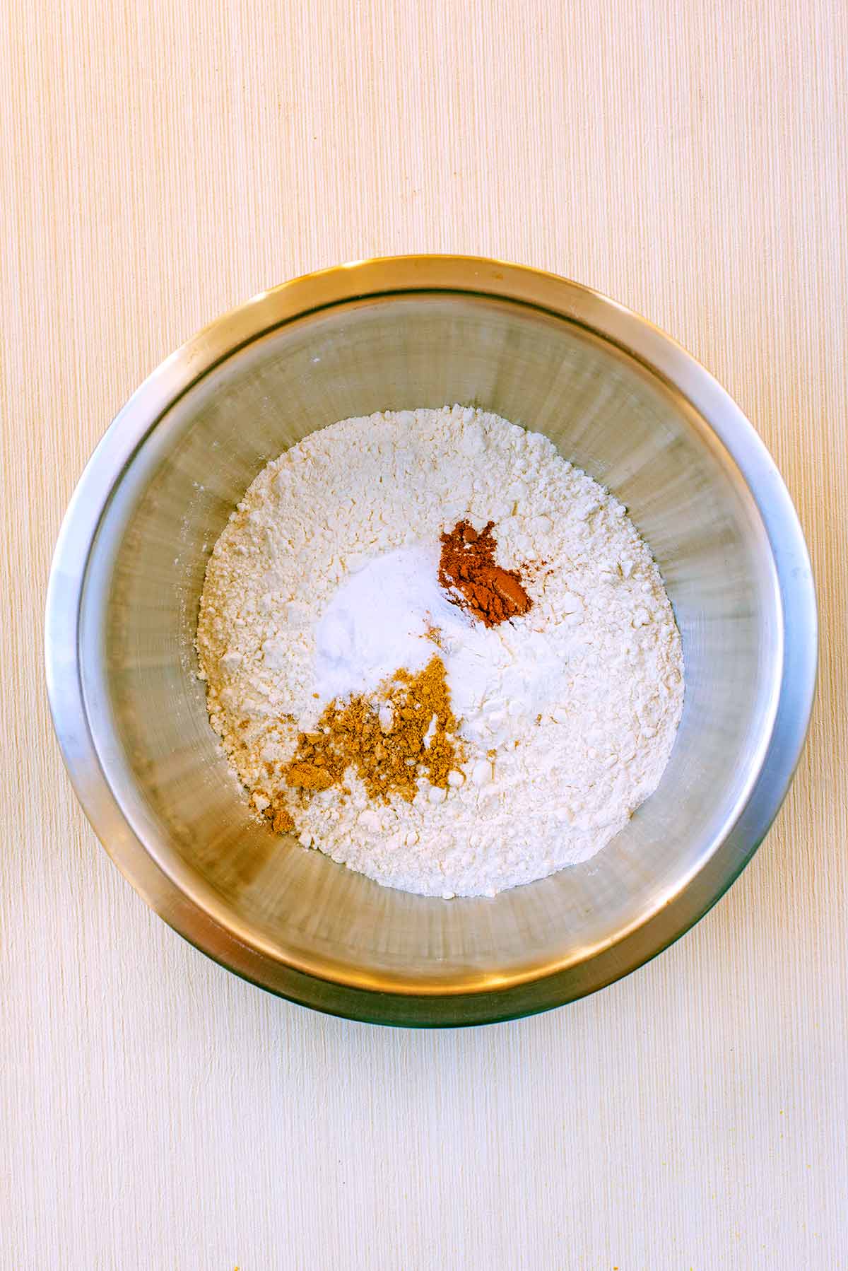 A mixing bowl containing flour, baking powder, baking soda, cinnamon, ginger and salt.