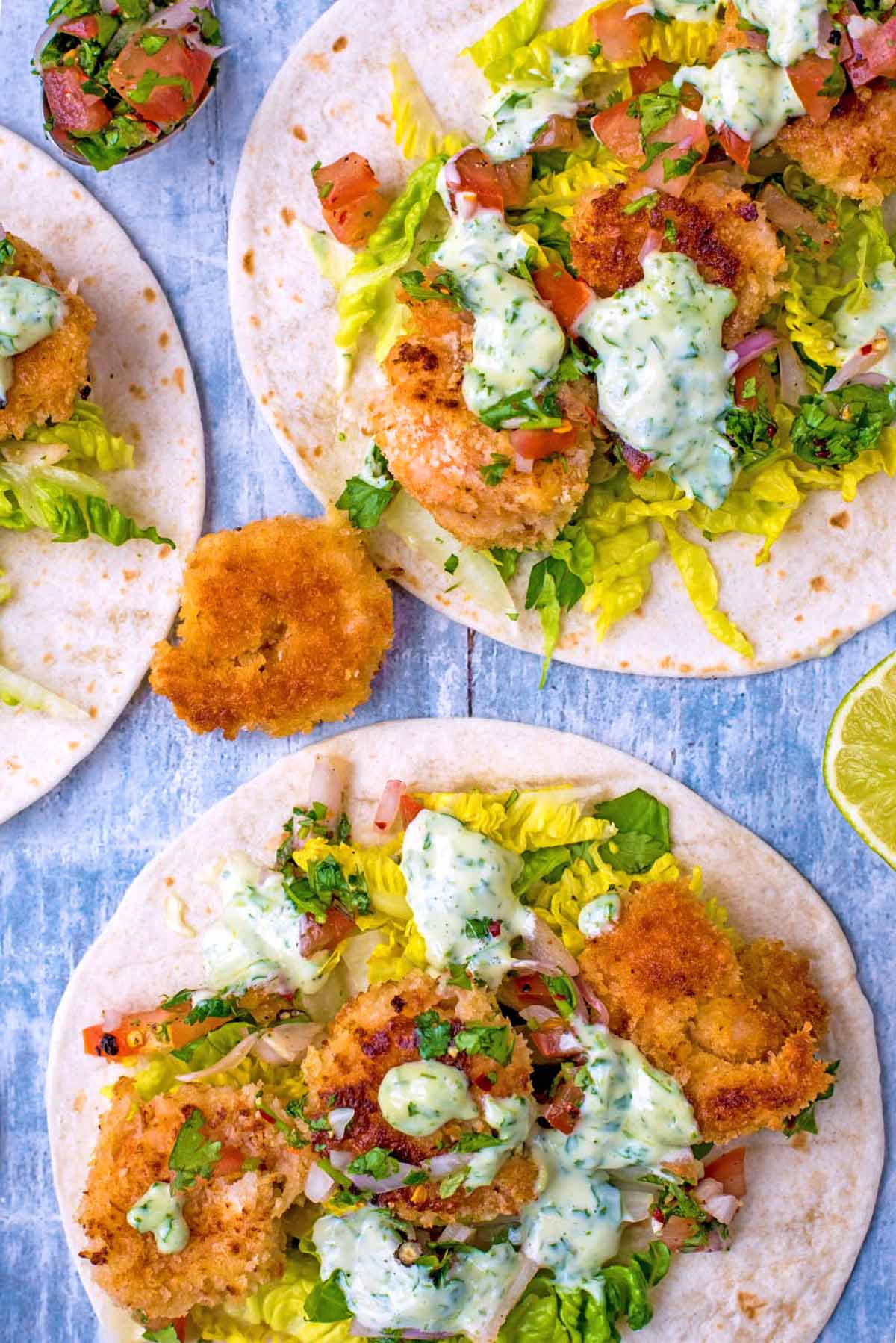 Crispy Prawn Tacos with lettuce and salsa with a drizzle of creamy sauce.
