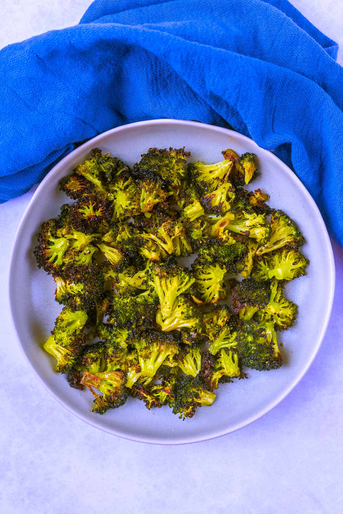 A plate of roasted broccoli next to a blue towel.