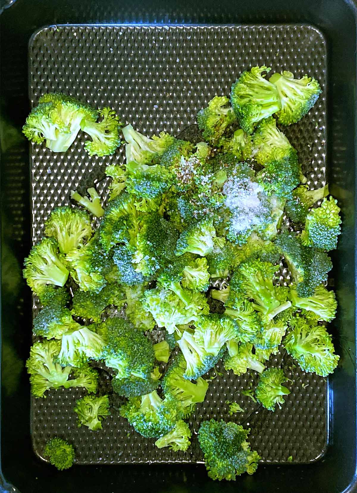 Broccoli florets in a baking tray with oil and seasoning.