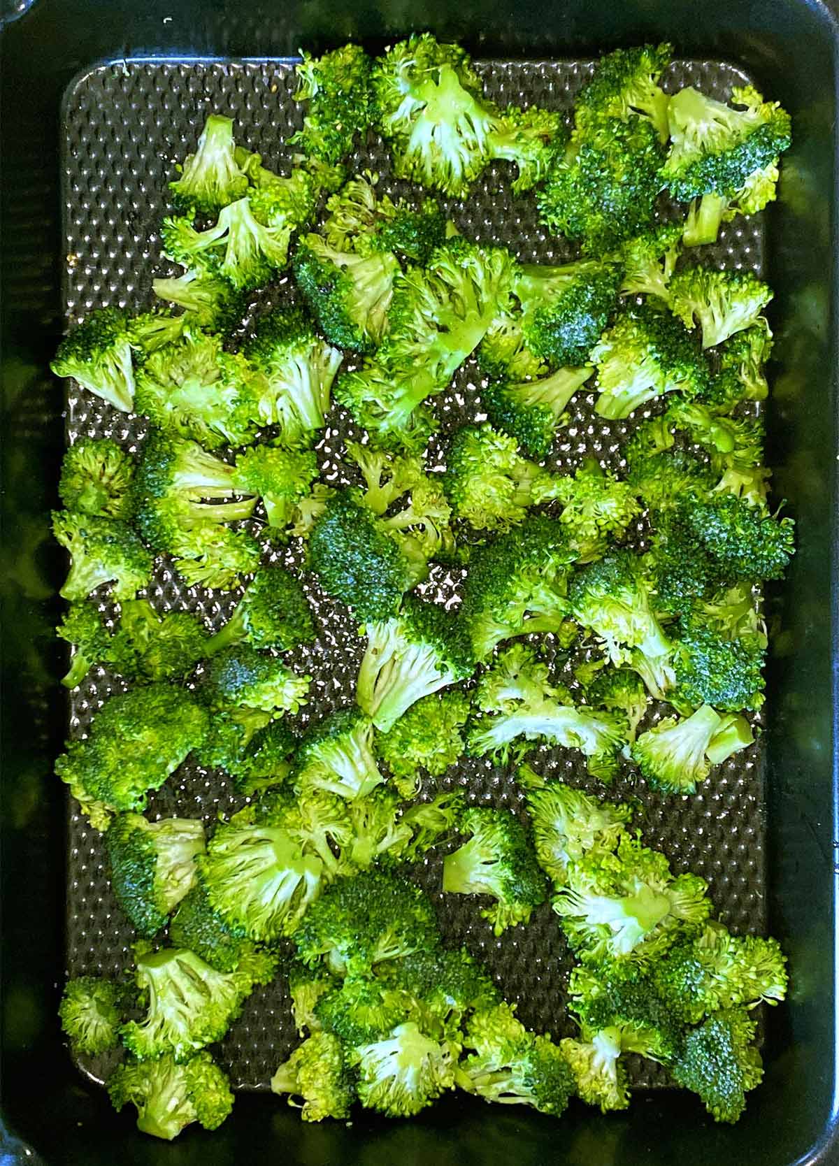 Coated broccoli florets spread over a baking tray.