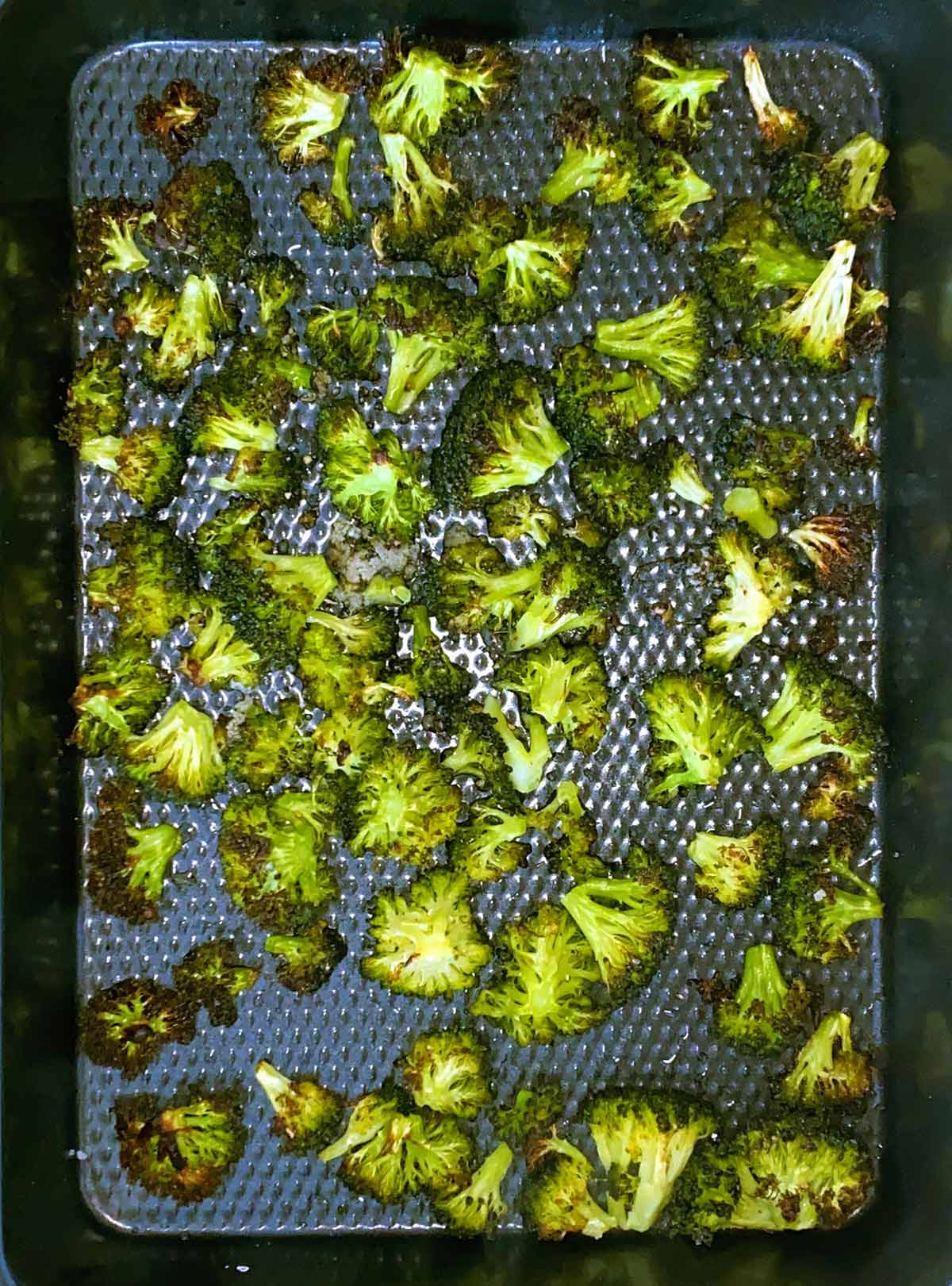 A baking tray covered in roasted broccoli florets.