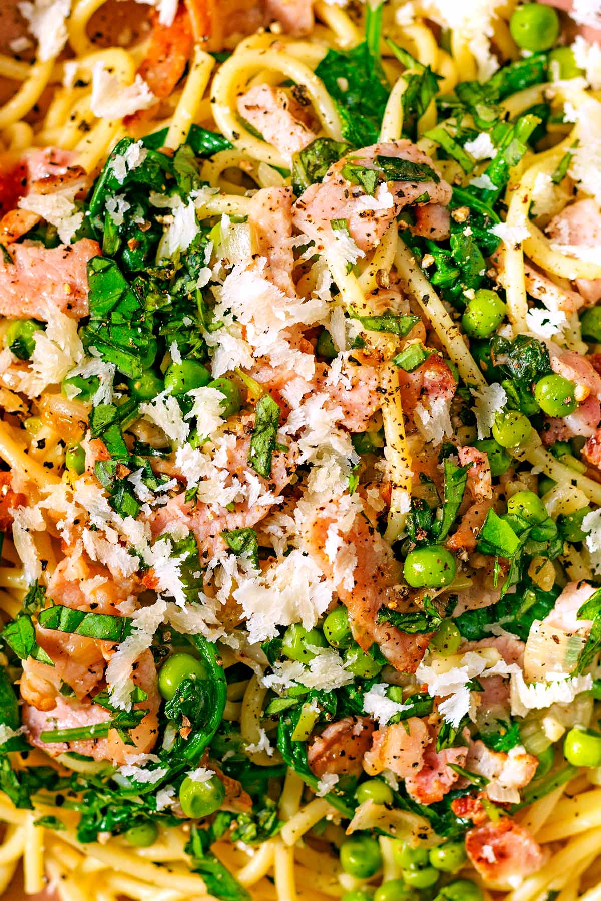 Bacon, peas and spinach mixed into cooked spaghetti with herbs and Parmesan shavings on top.
